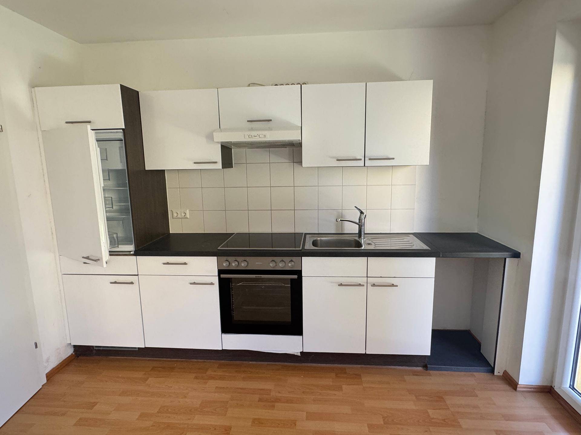 Einbauküche mit weißen Schränken, schwarzer Arbeitsplatte und offenem Kühlschrank.