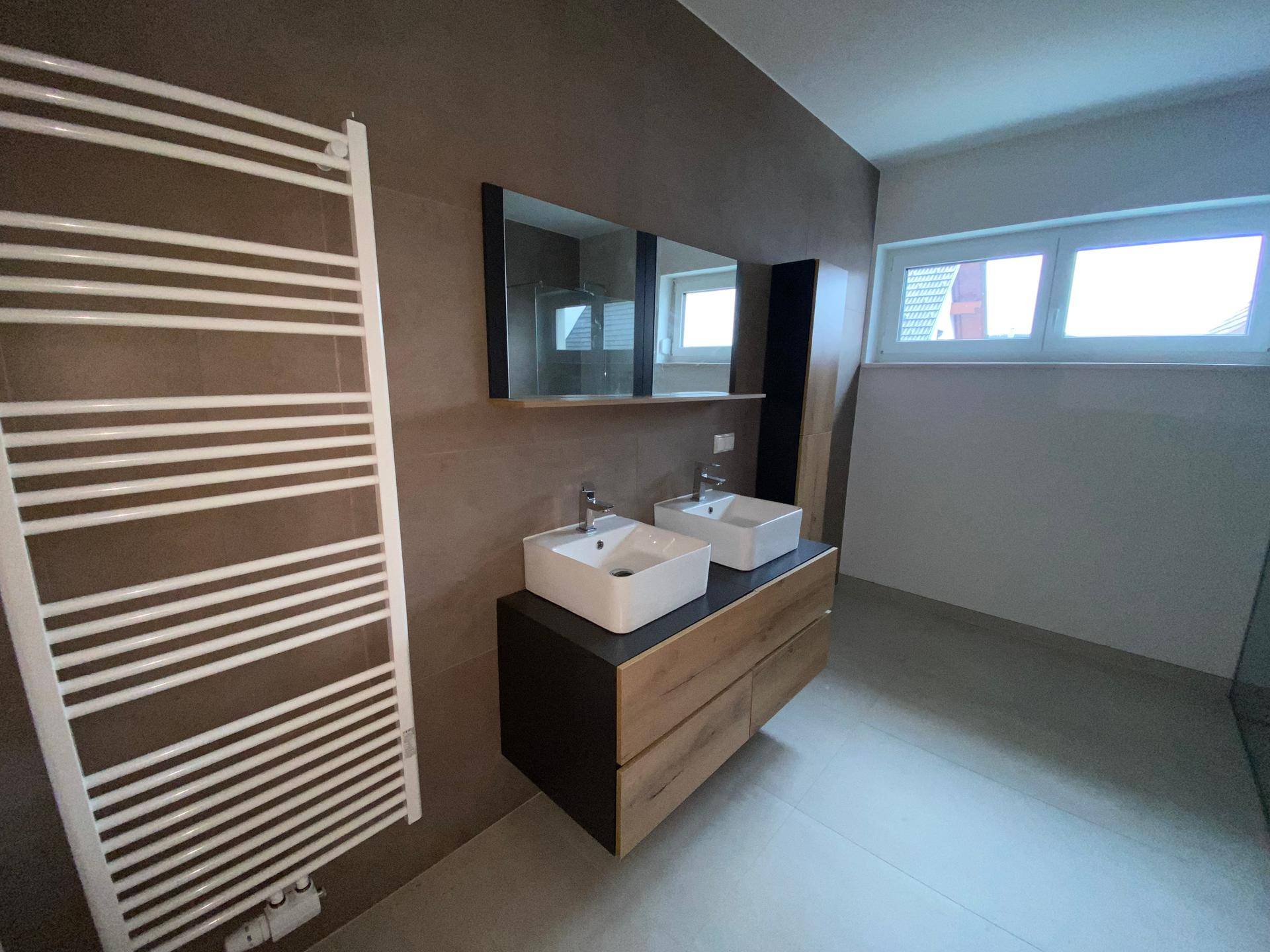 Helles Badezimmer mit Doppelwaschbecken, beheiztem Handtuchhalter und Fenster.