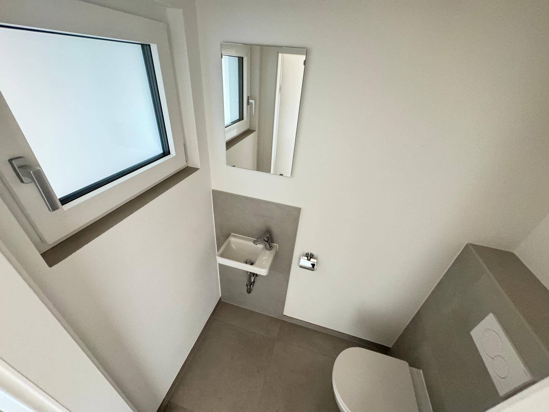Helles Gäste-WC mit Fenster, modernem Wand-WC und kleinem Waschbecken.