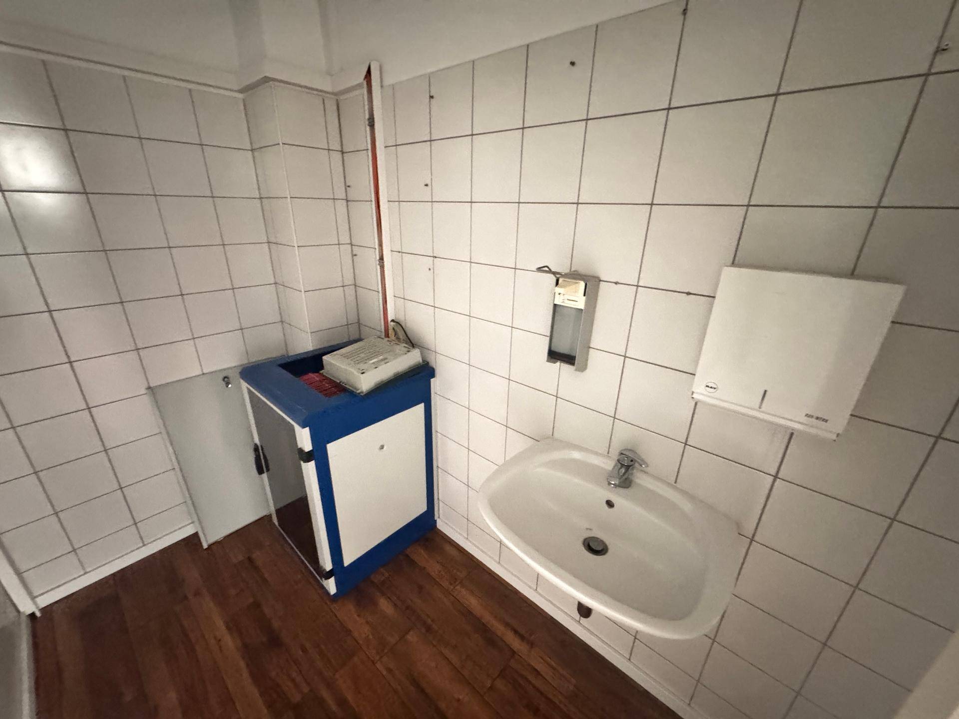 Einfaches WC mit weiß gefliesten Wänden, einem Waschbecken und einem Spender.