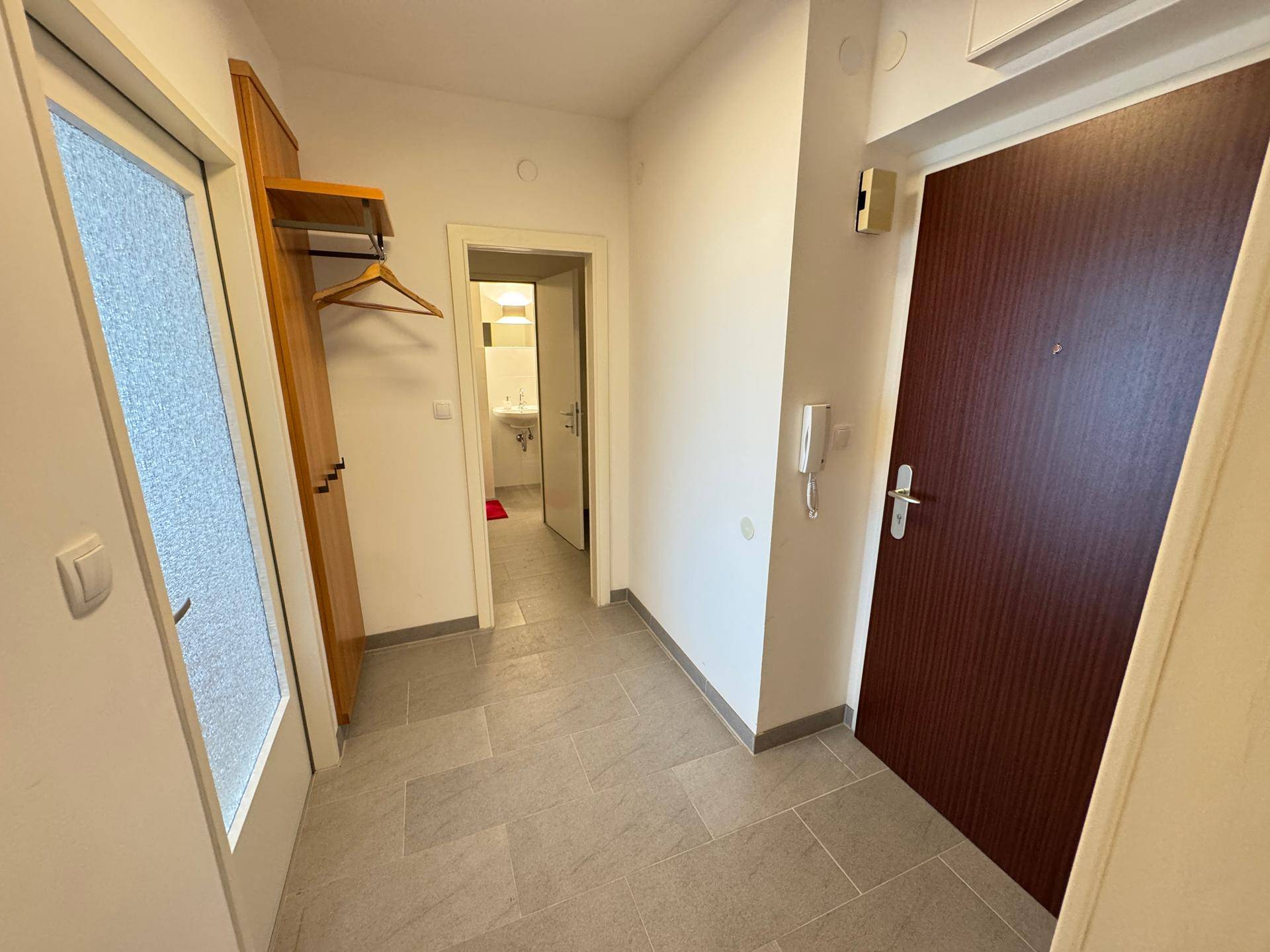Heller Flur mit Fliesenboden, Holzgarderobe und Zugang zu einem Badezimmer.