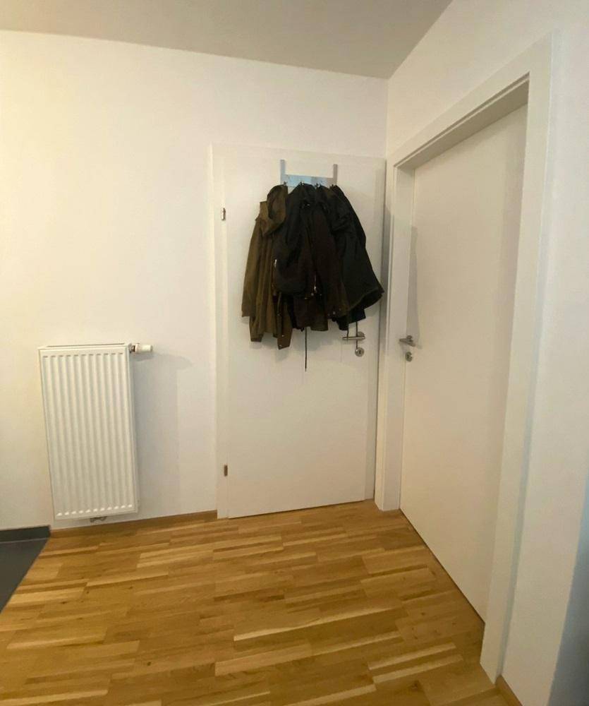 Eingangsbereich mit Holzboden, weißer Tür und Heizkörper.