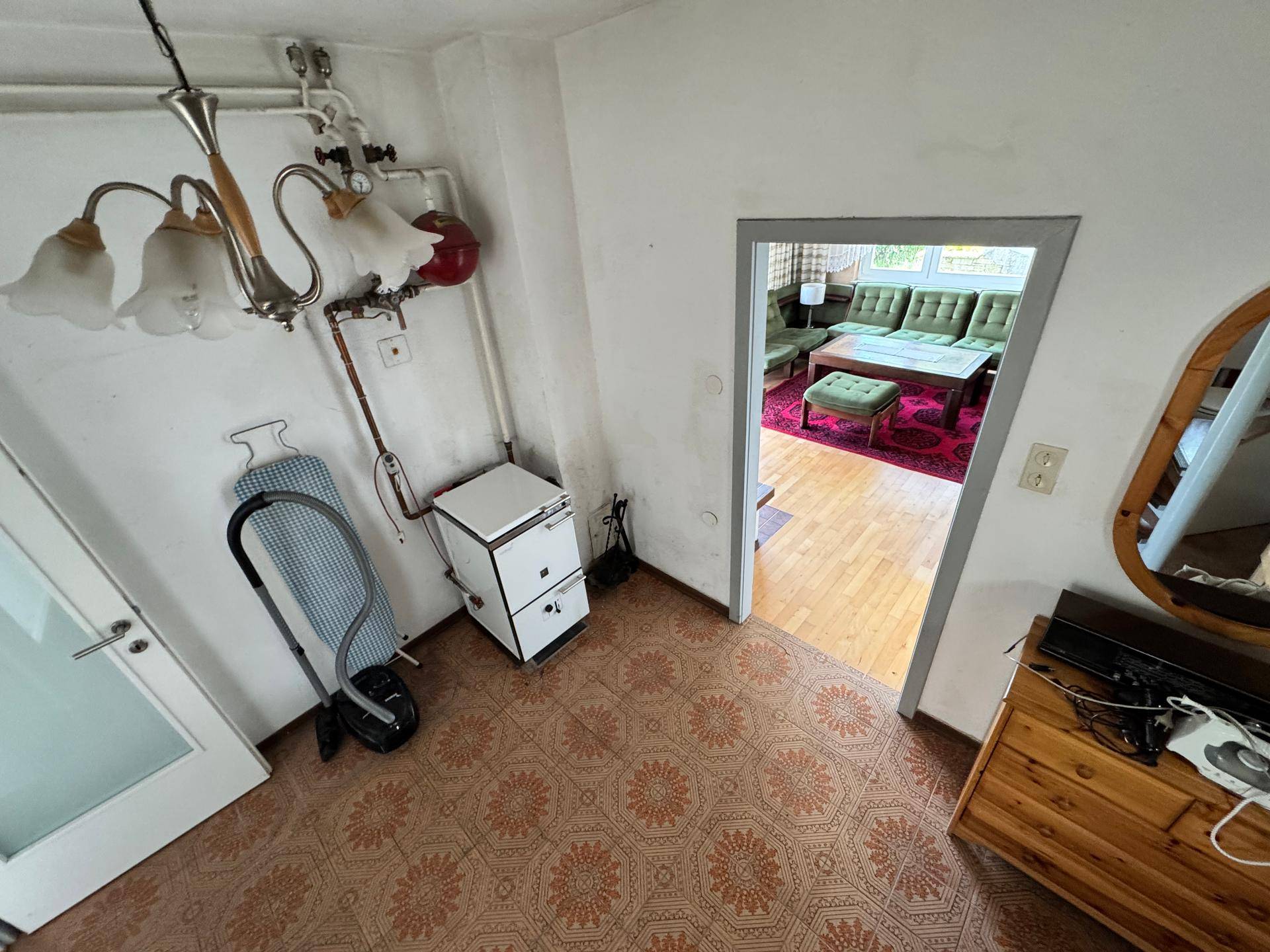 Flur mit Heizungsanlage, gemustertem Boden und Blick in das Wohnzimmer.
