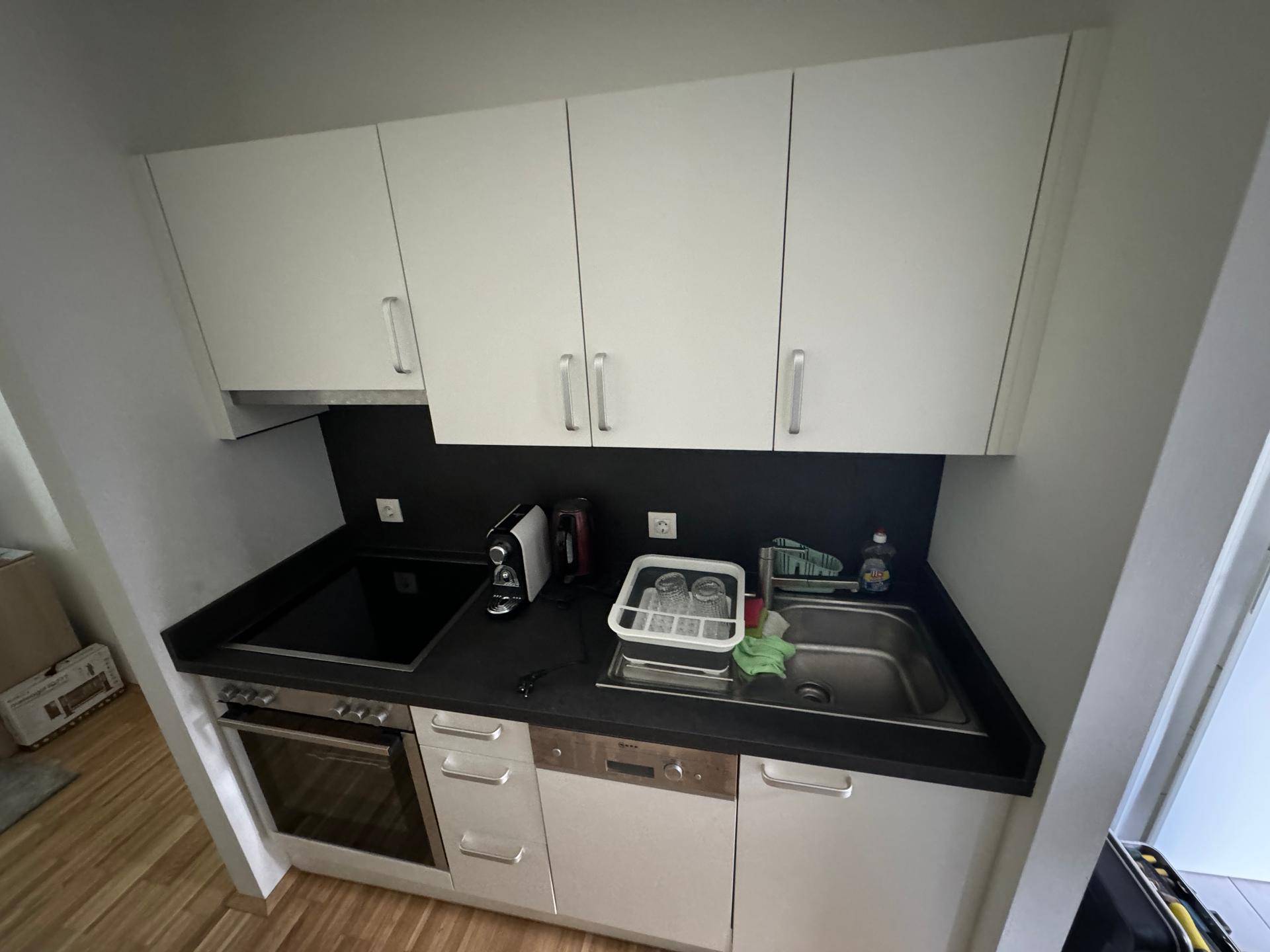 Moderne Einbauküche mit weißen Schränken, dunkler Arbeitsplatte und integrierten Geräten.