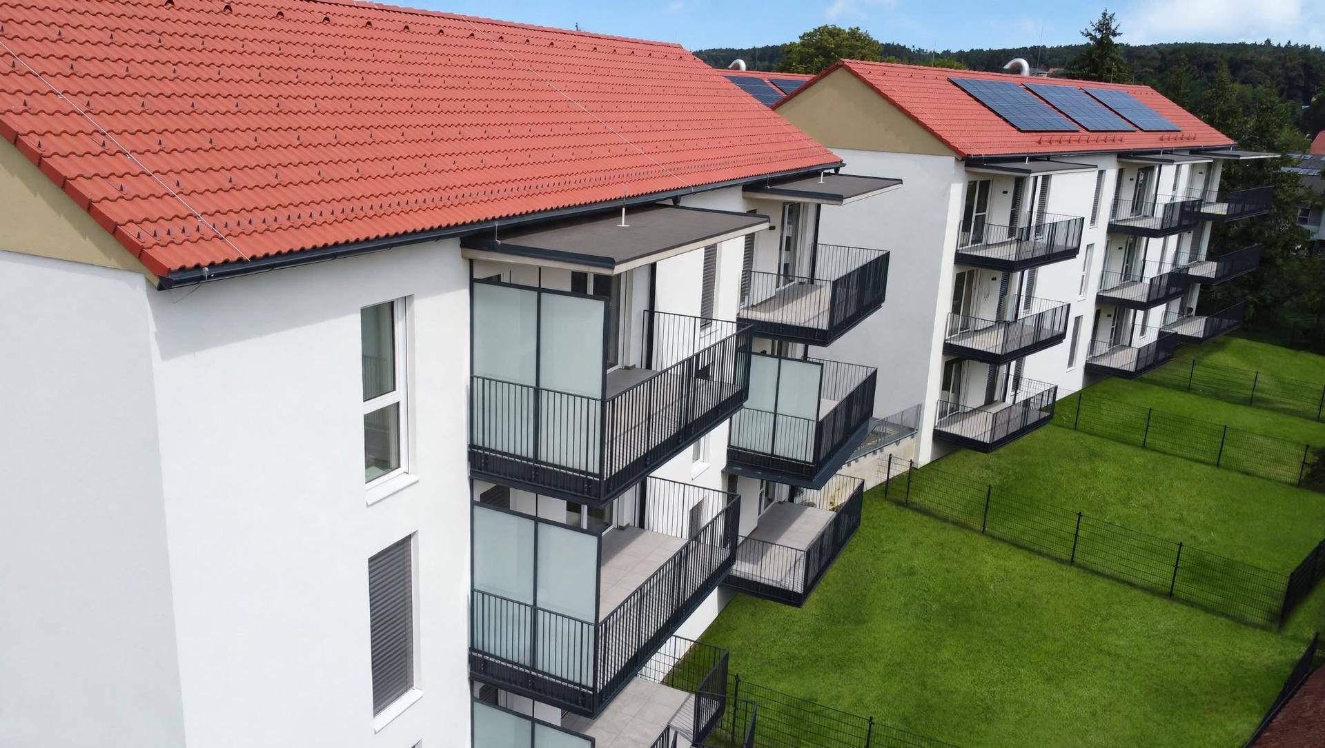 Nahaufnahme der modernen Wohngebäude mit weißen Fassaden, roten Ziegeldächern, Balkonen und Solaranlagen.