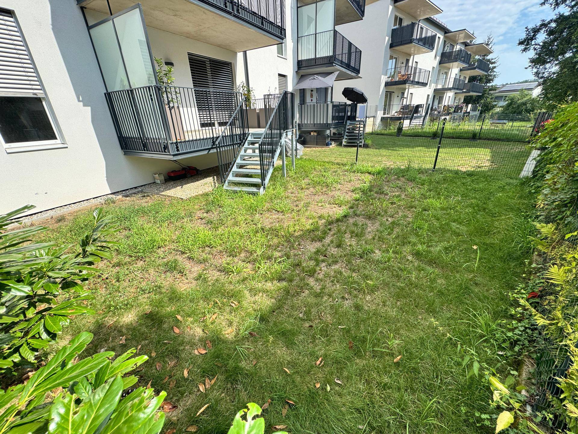 Private Gartenfläche mit Rasen und Zaun, direkt an der Wohnanlage gelegen.