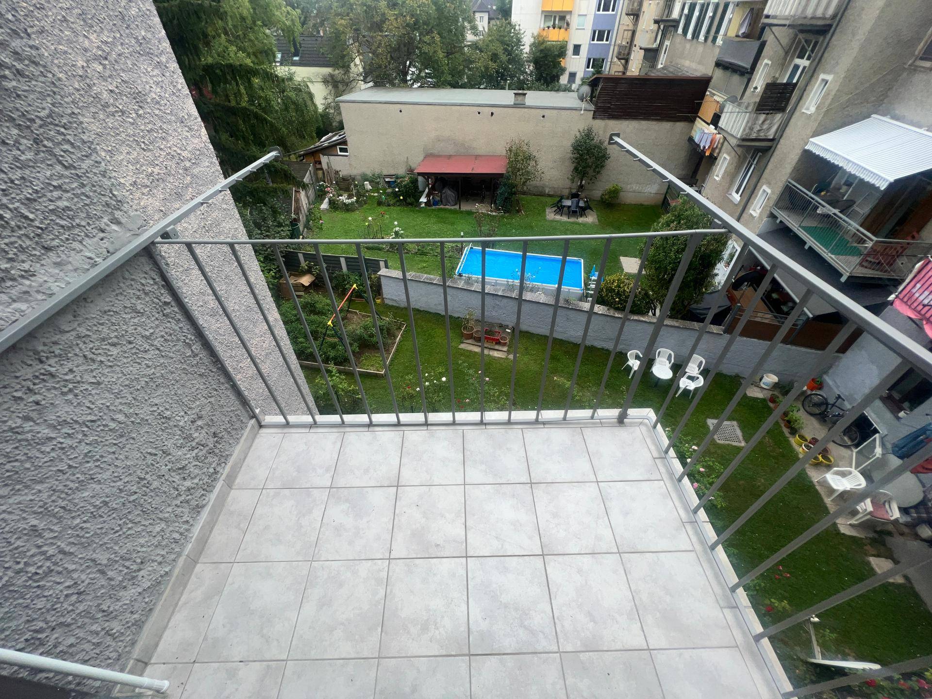 Gefliester Balkon mit Metallgeländer und Blick auf den Gemeinschaftsgarten.