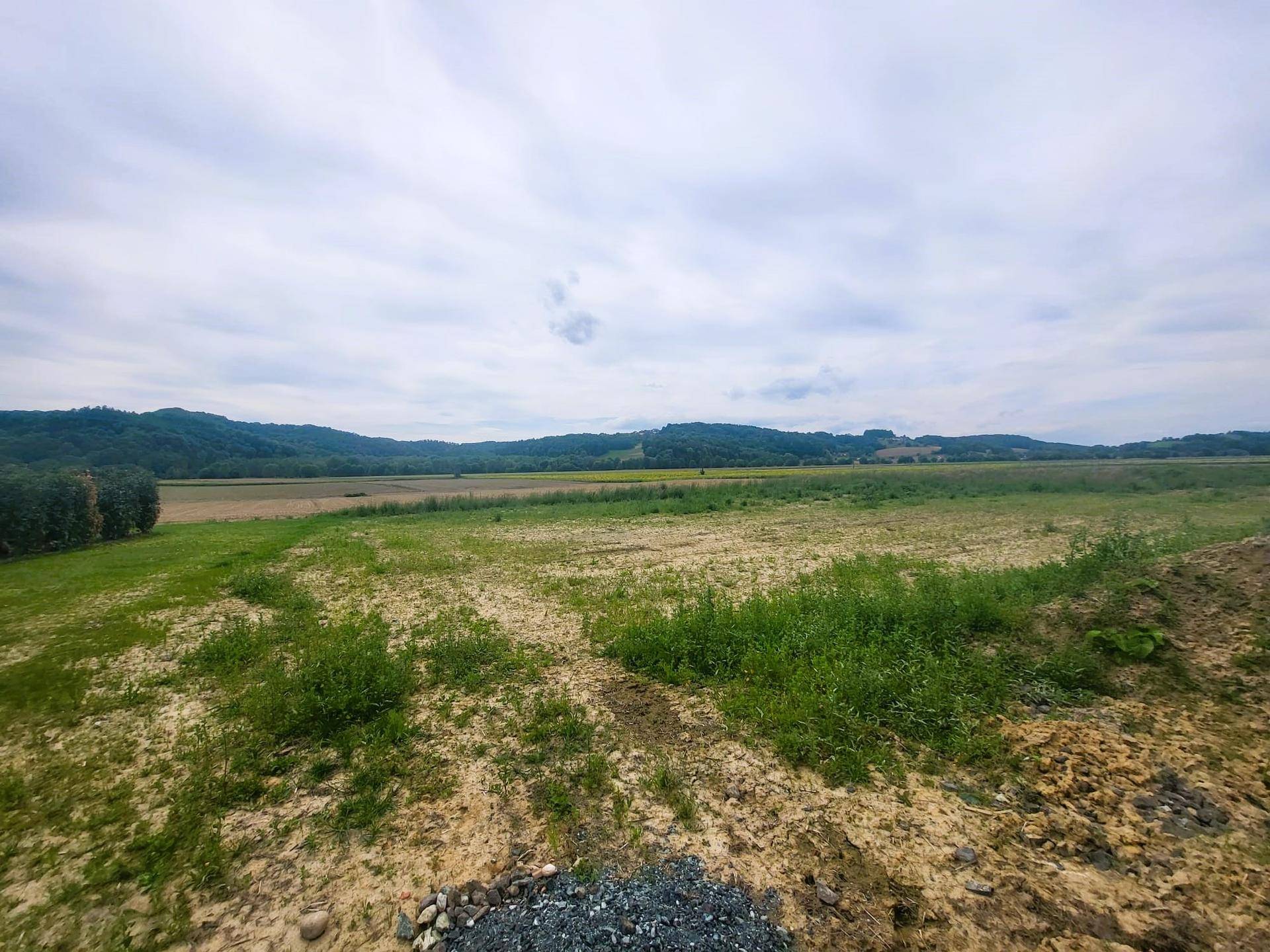 Offene Felder und grüne Hügel unter einem weiten, bewölkten Himmel.