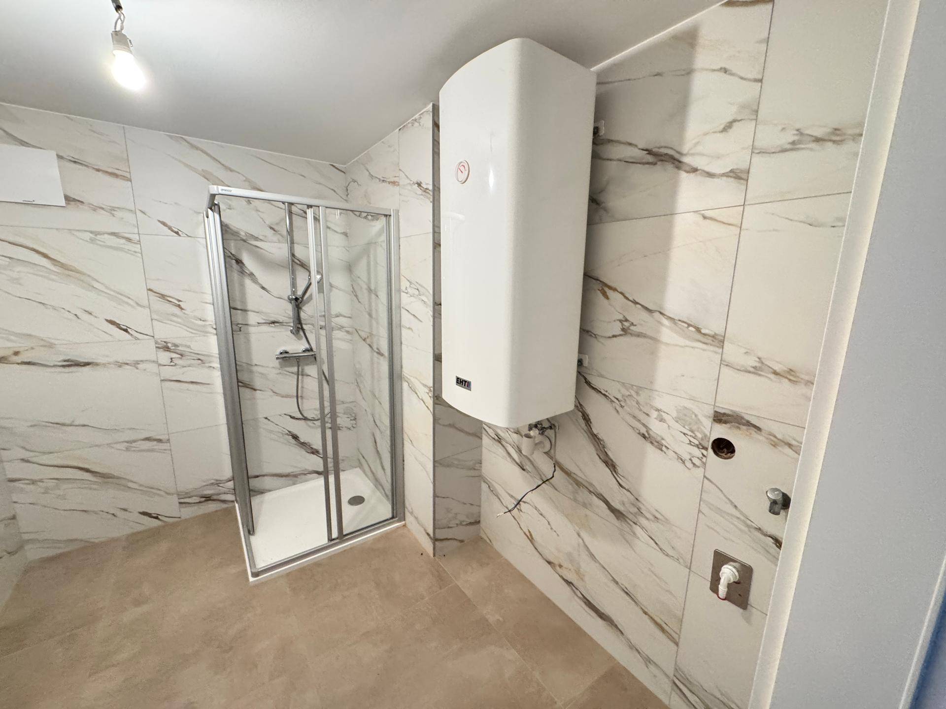 Badezimmer in Renovierung mit Marmoroptik-Fliesen, Duschkabine und Heizkörper.