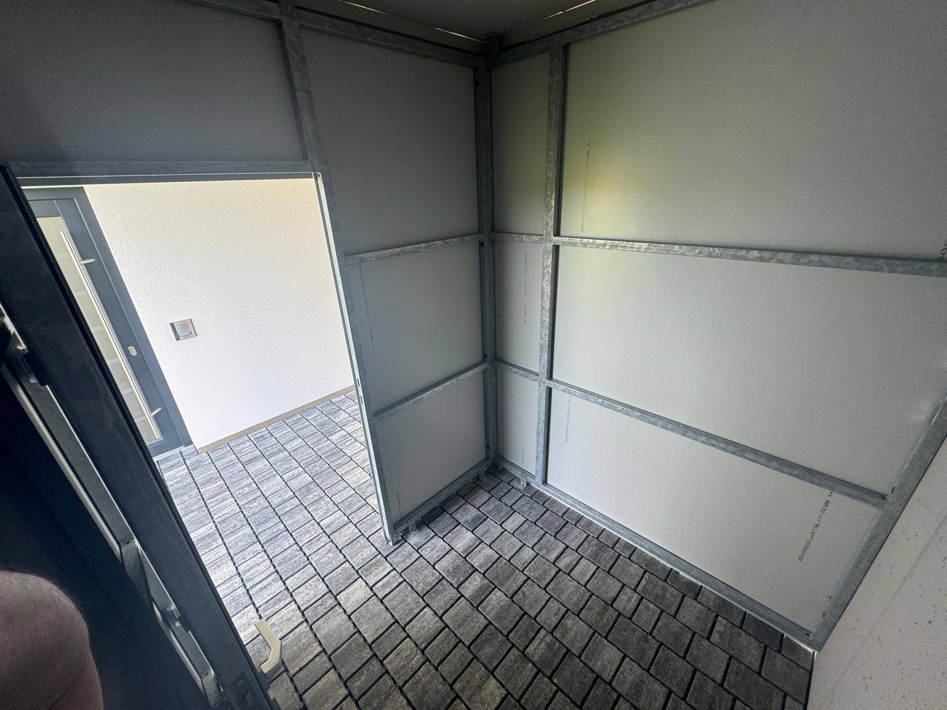 Praktischer Abstellraum im Carportbereich mit gepflastertem Boden.