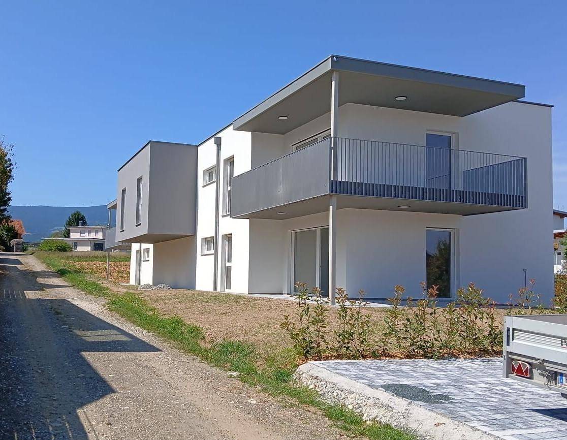Modernes Neubaugebäude mit weißer Fassade, grauen Akzenten und Balkonen unter blauem Himmel.