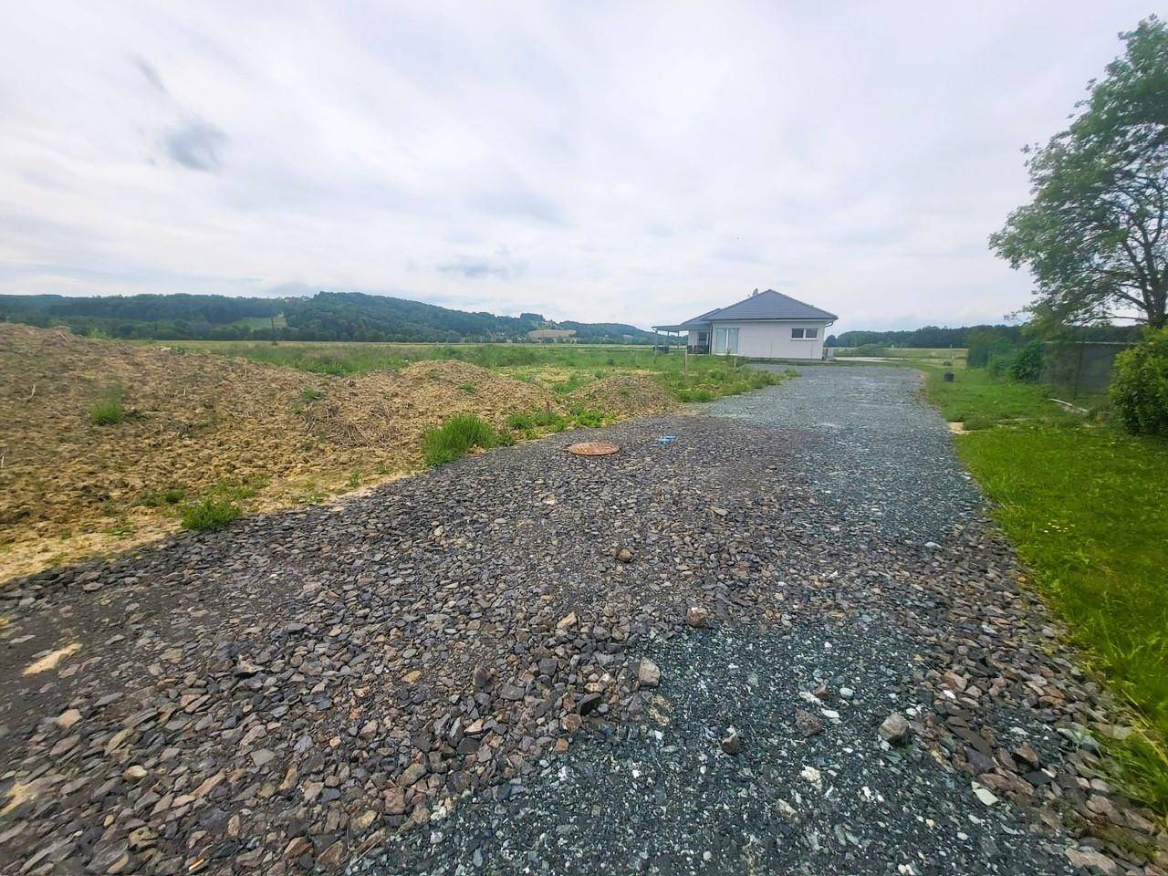 Schotterweg führt zu einem Haus in ländlicher Umgebung mit Hügeln im Hintergrund.