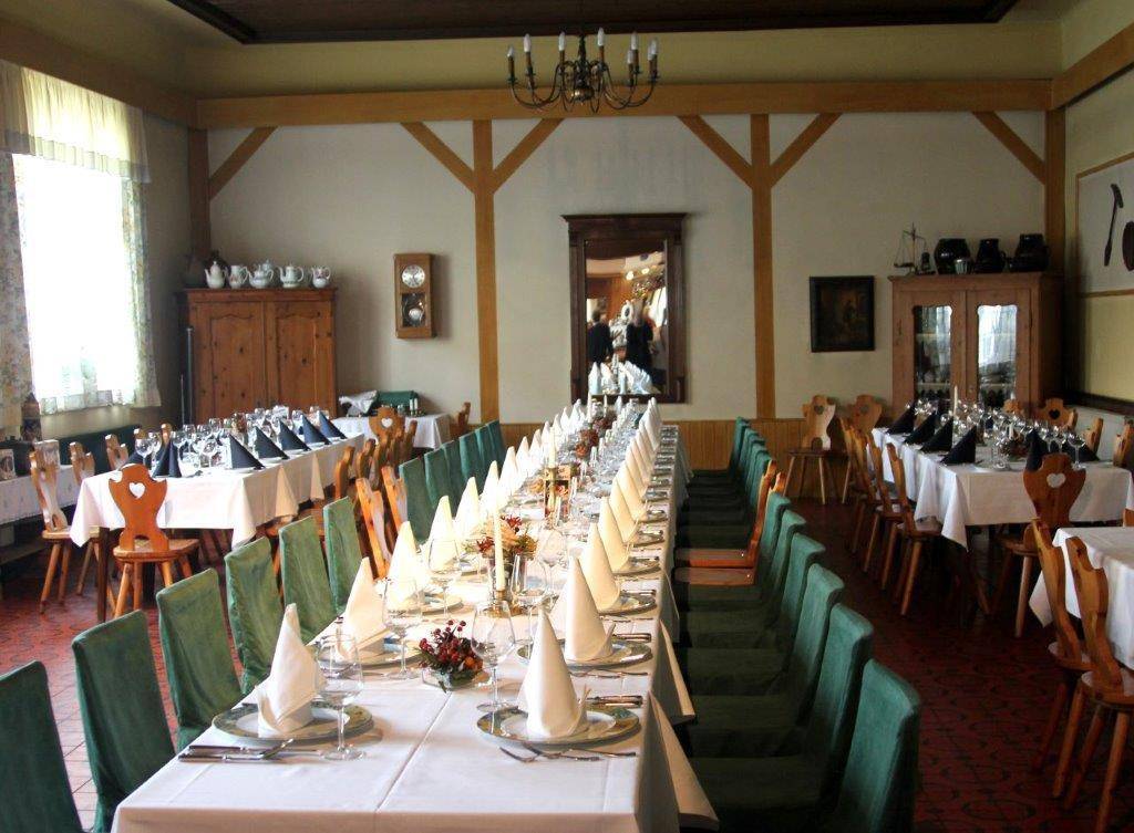 Großer Speisesaal mit langen Tischen, grünen Stühlen und Holzbalken an der Decke.