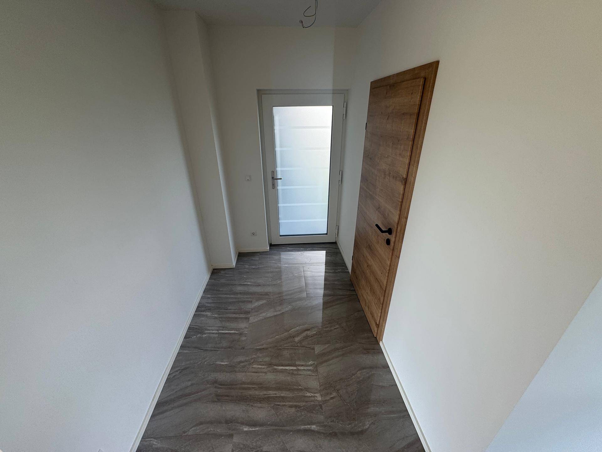 Heller Eingangsbereich mit modernen grauen Fliesen und einer Holztür.