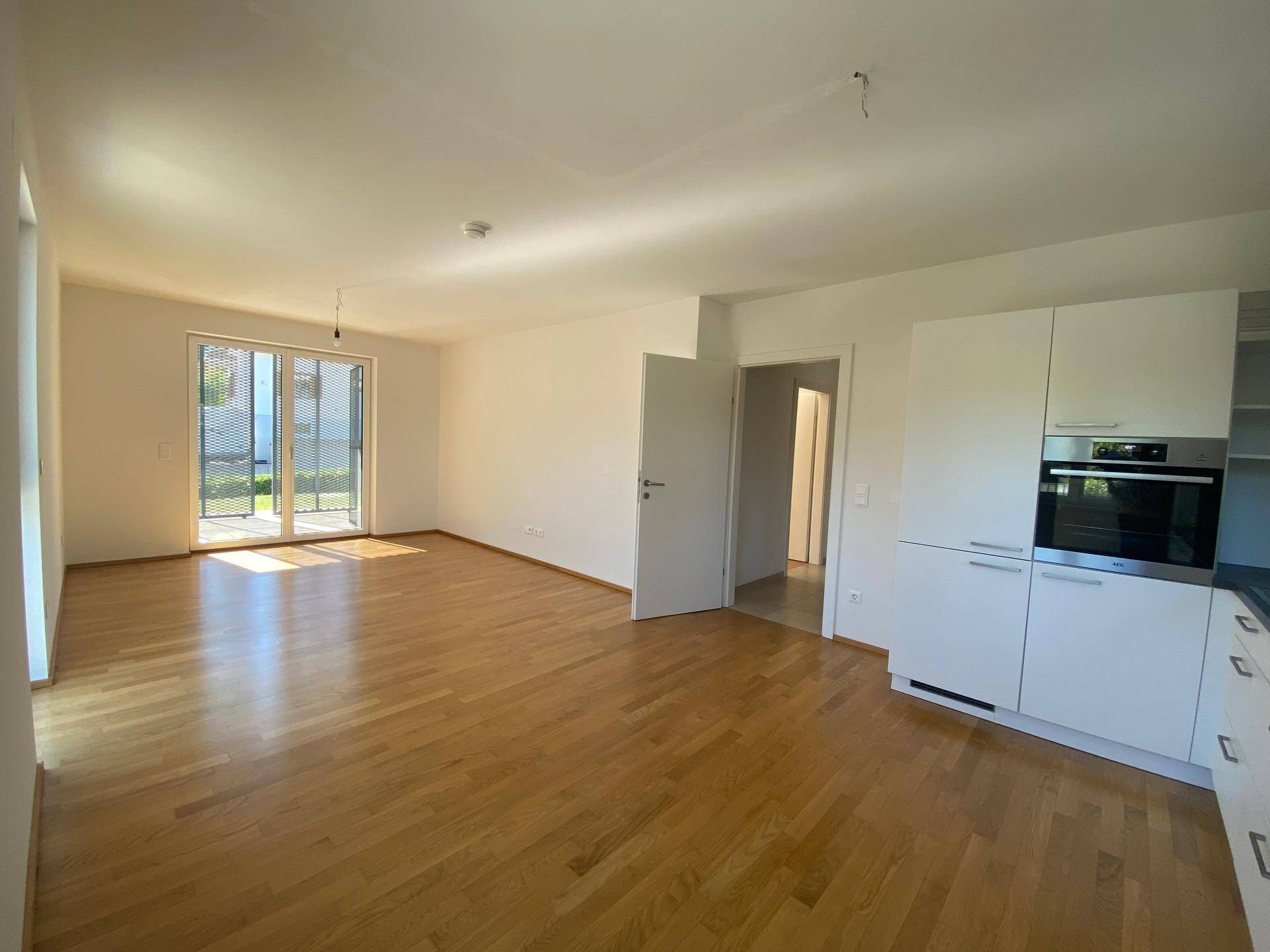 Offener Wohnbereich mit Holzboden und Zugang zur Terrasse, inklusive integrierter Küchenzeile.