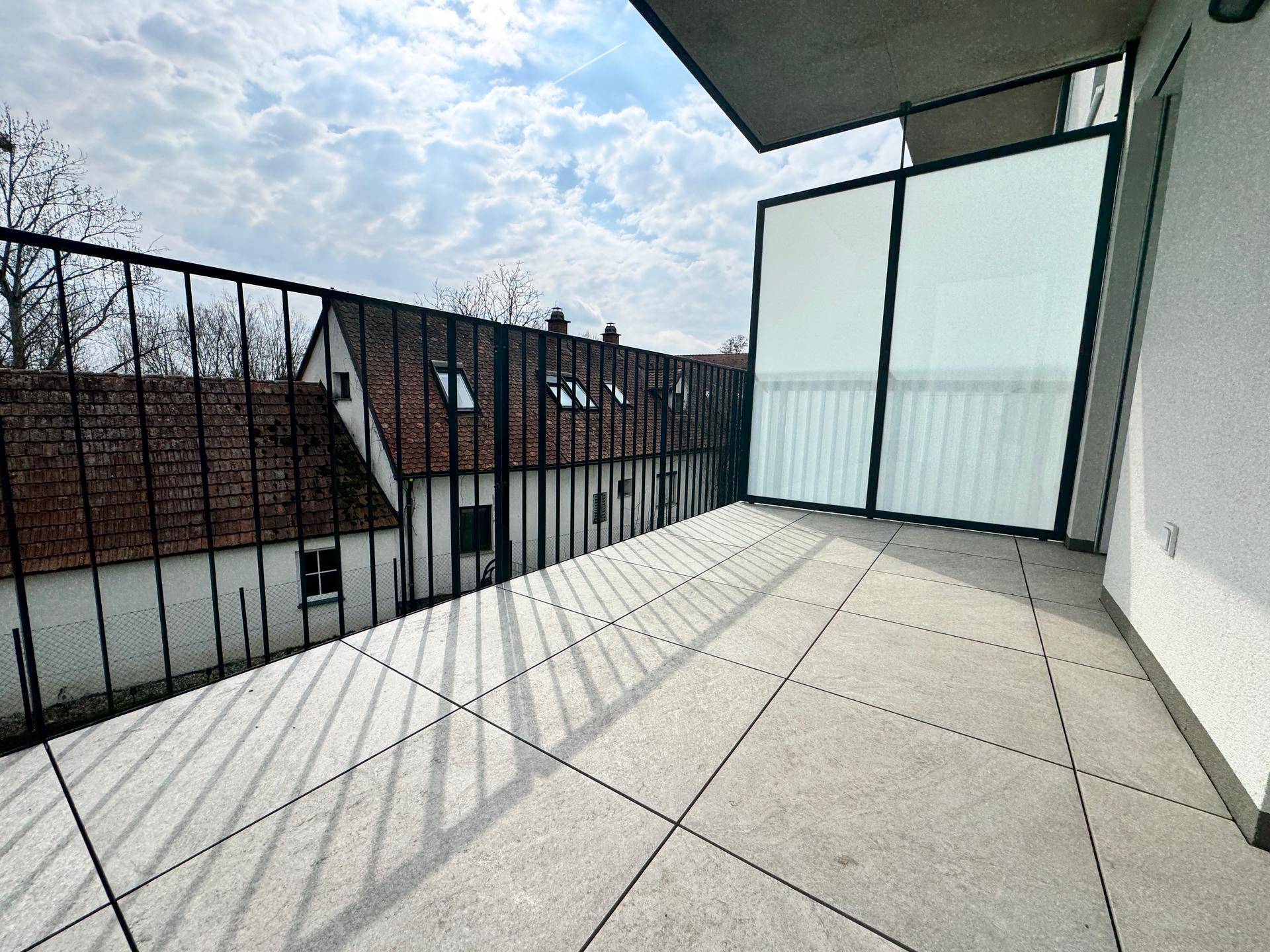 Geräumiger Balkon mit modernen Fliesen und Blick auf die umliegenden Häuser und den Himmel.