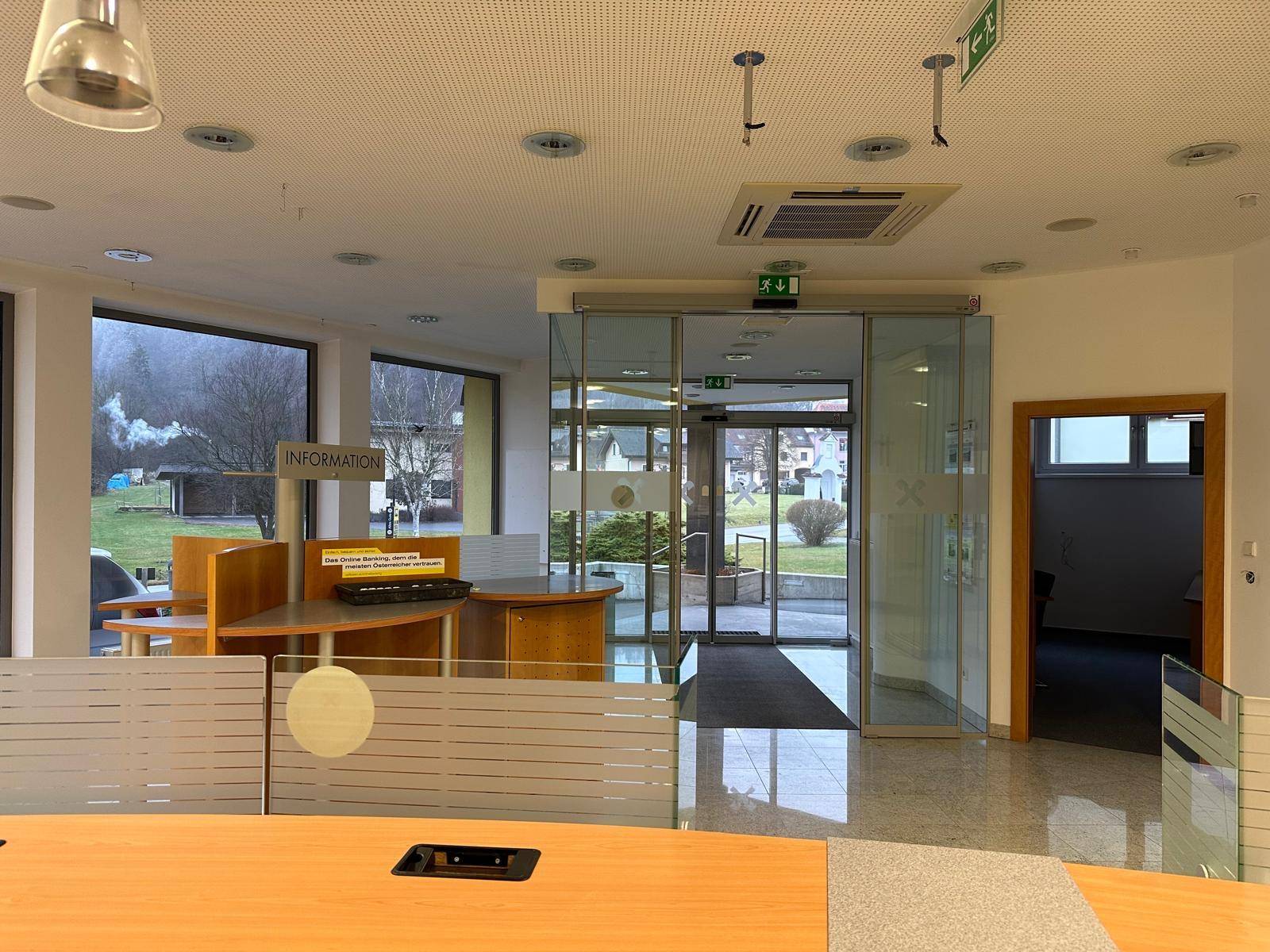 Offener Bürobereich mit Schaltern, großen Fenstern und Blick auf den Außenbereich.