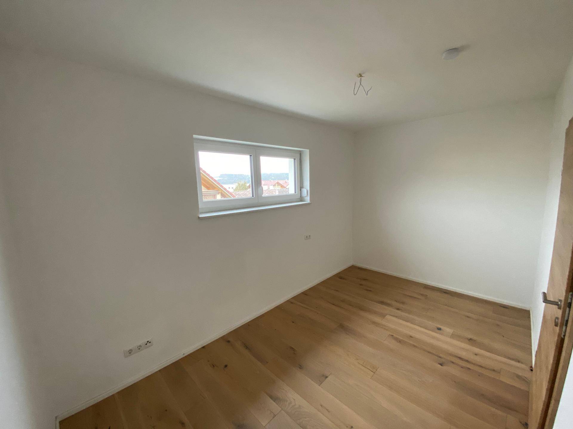 Helles Schlafzimmer mit Holzboden und Fenster, das einen Blick nach draußen ermöglicht.