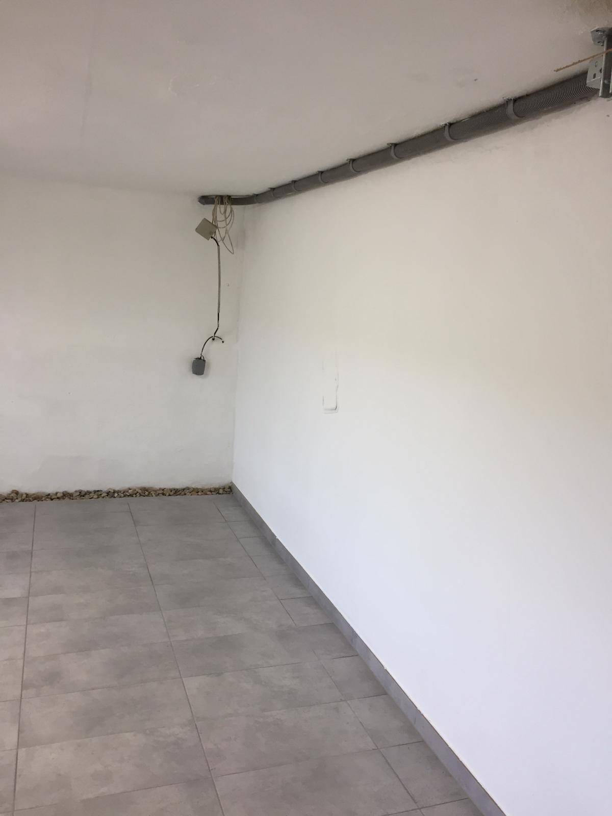 Einfacher Kellerraum mit Fliesenboden und sichtbaren Leitungen an der Decke.