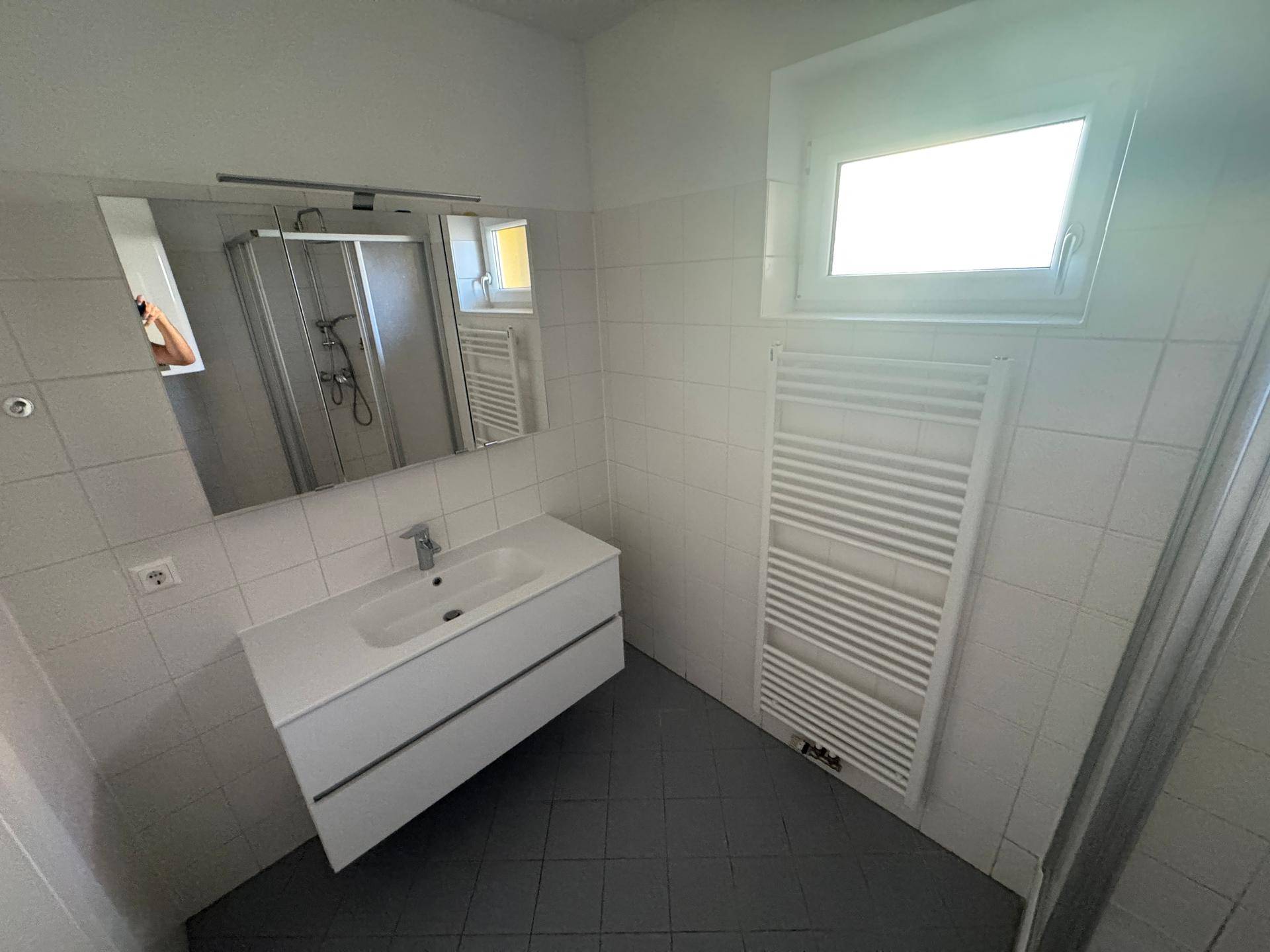 Helles Badezimmer mit modernem Waschbeckenunterschrank, Spiegel und beheiztem Handtuchhalter.