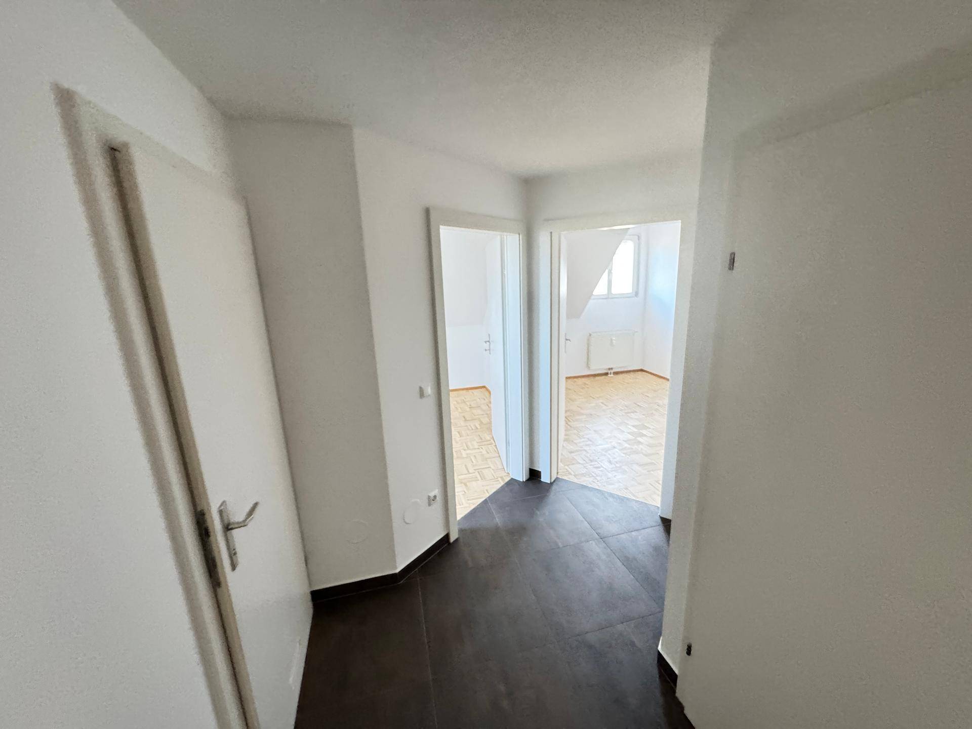 Heller Flur mit dunklen Fliesen und Zugang zu mehreren Zimmern im Dachgeschoss.