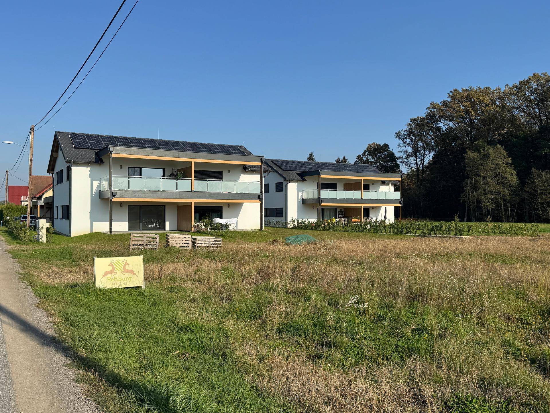 Zwei moderne Doppelhaushälften mit Solaranlagen und unbebauten Gärten in ländlicher Umgebung.