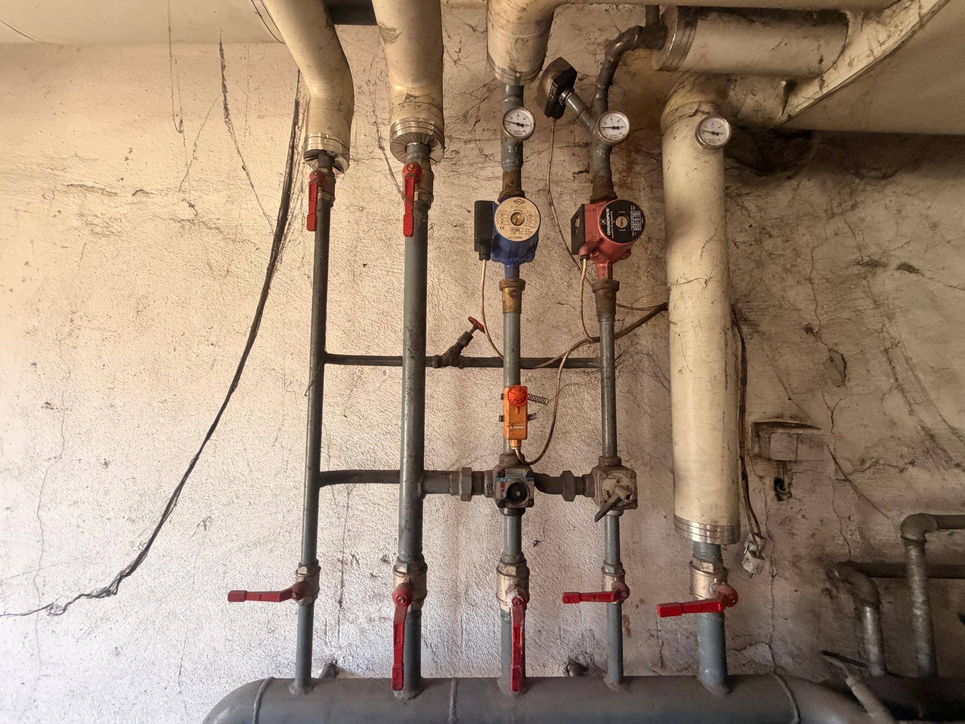 Heizungsanlage mit zahlreichen Rohren und Ventilen in einem älteren Technikraum.