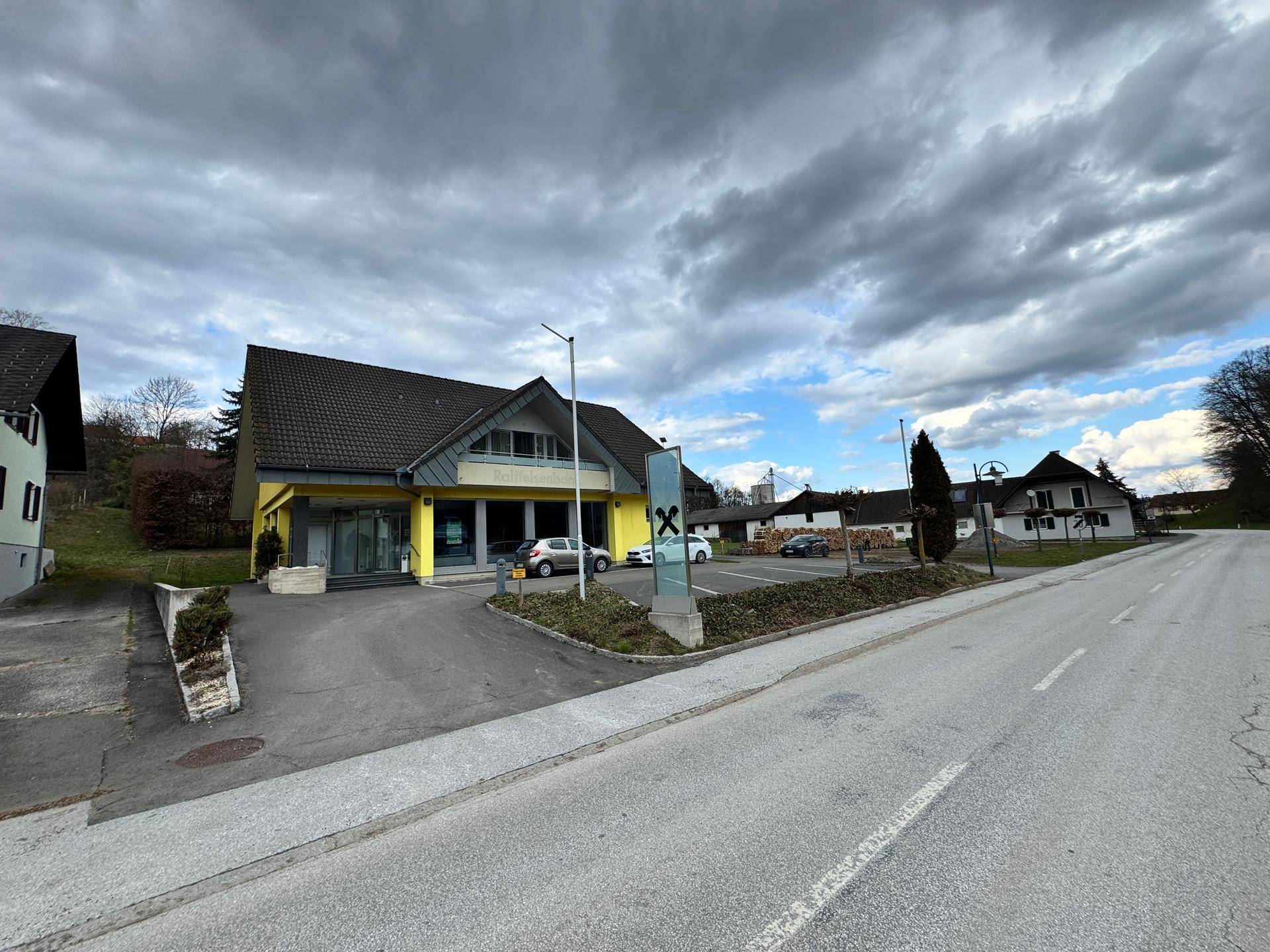 Gelbes Gebäude mit Satteldach und Parkplatz an einer ländlichen Straße.