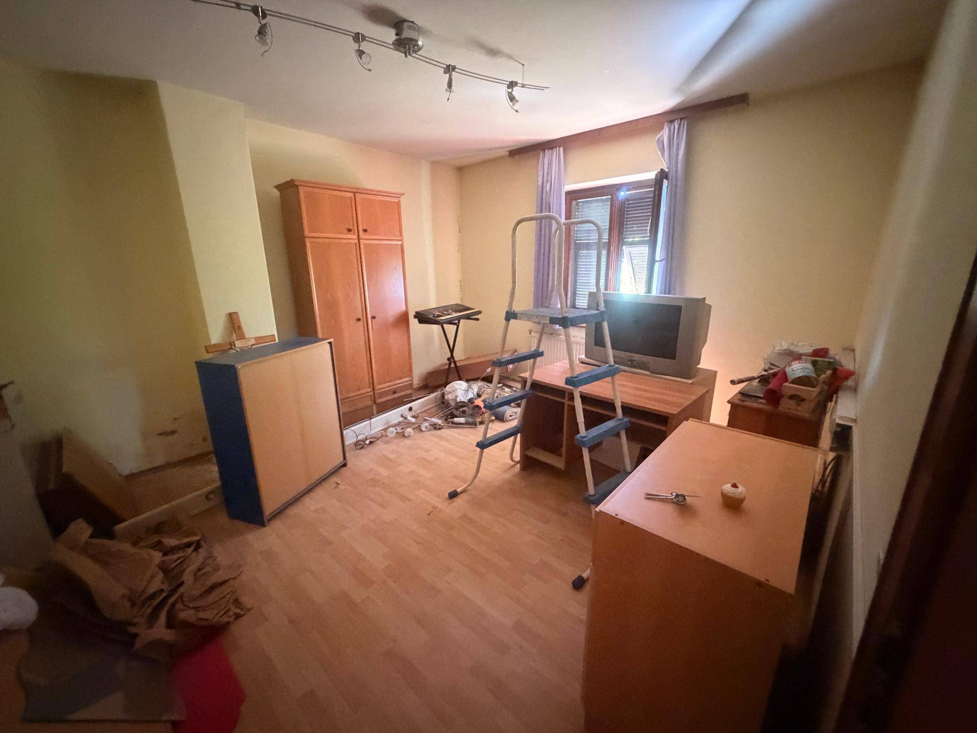 Zimmer mit Holzfußboden, Leiter und verschiedenen Gegenständen, möglicherweise in Renovierung.