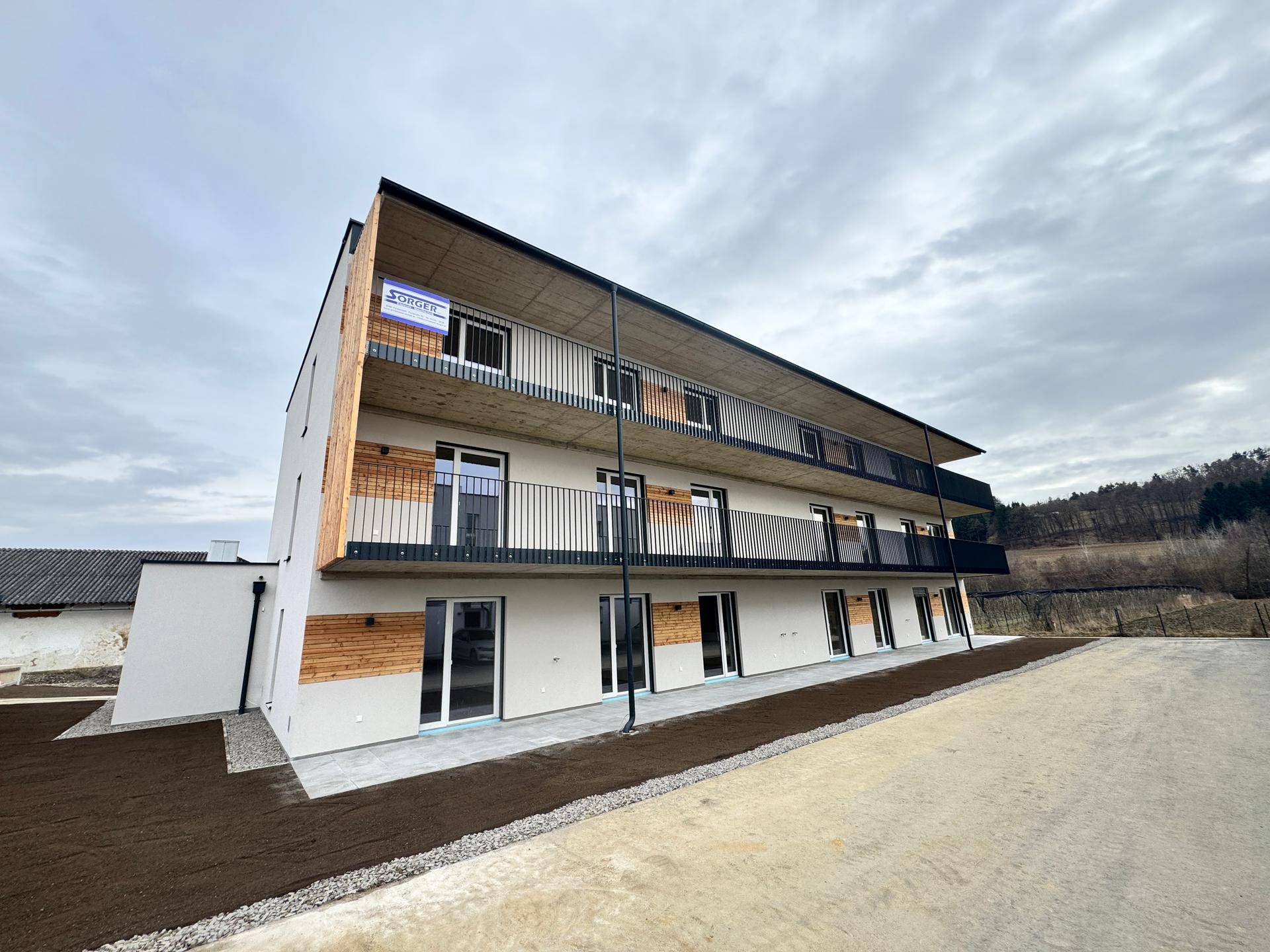 Neubau-Mehrfamilienhaus mit moderner Fassade, Balkonen und Holzverkleidung unter bewölktem Himmel.
