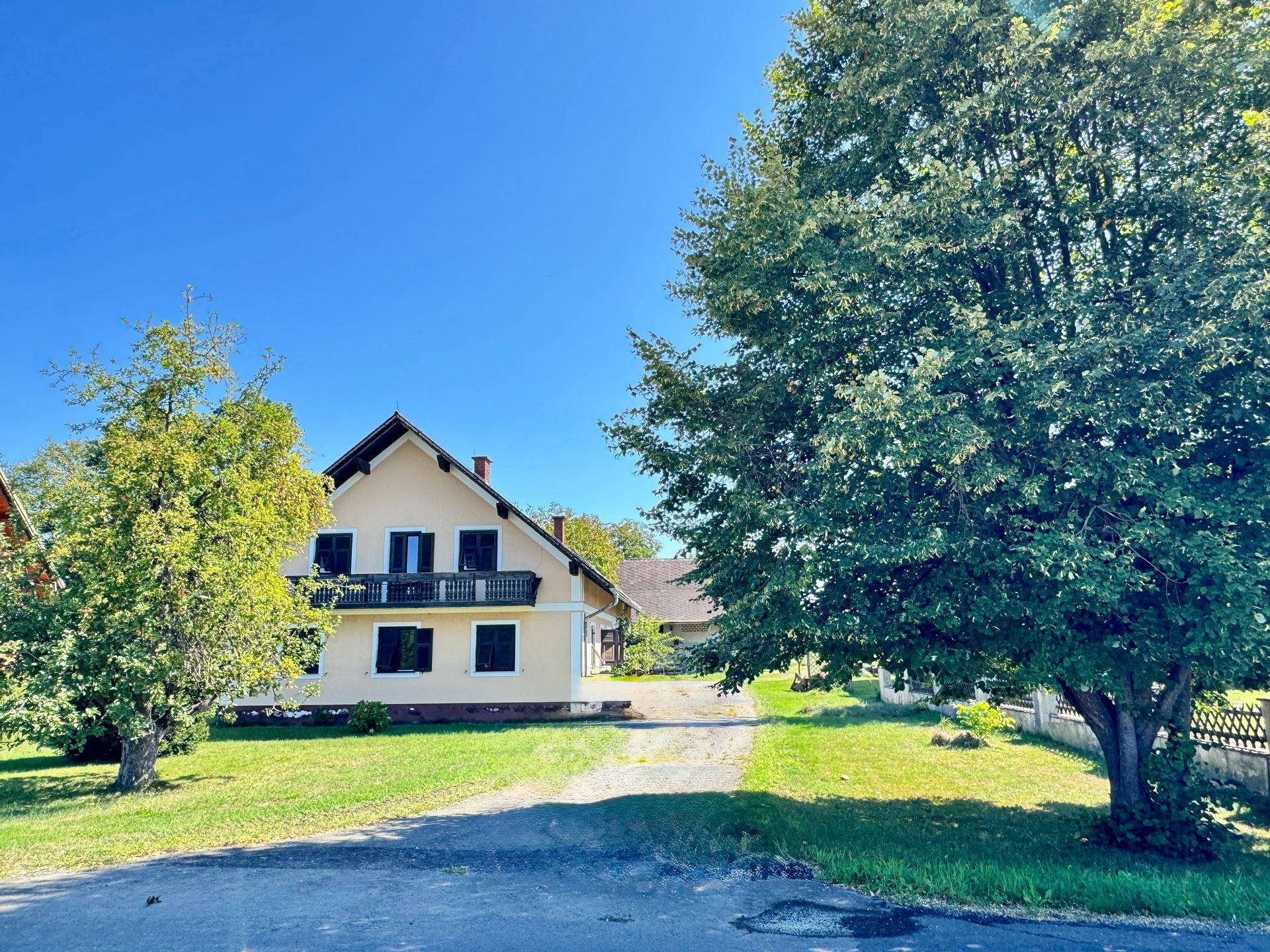 Großzügiges Landhaus mit Balkon und weitläufigem Grundstück unter blauem Himmel.