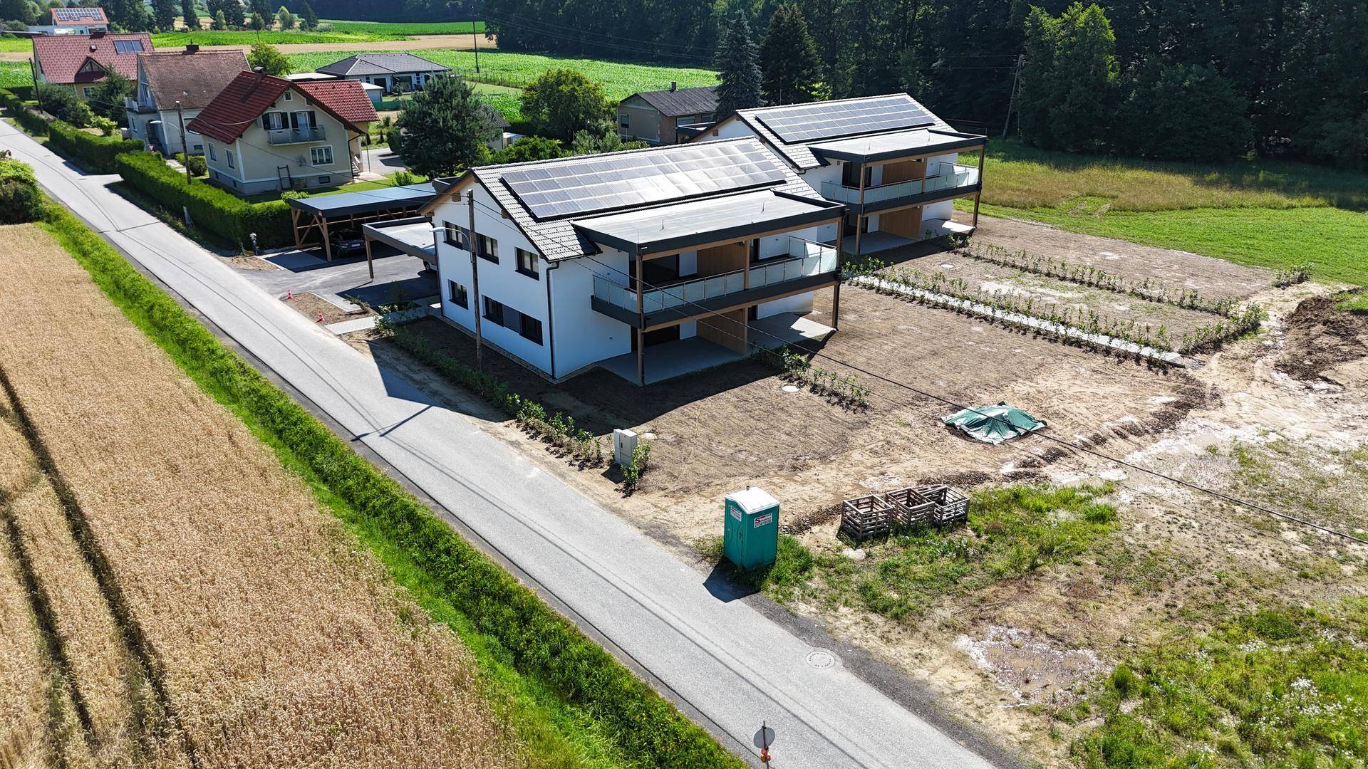 Luftaufnahme von zwei modernen Doppelhaushälften mit Solaranlagen und Carports an einer Landstraße.