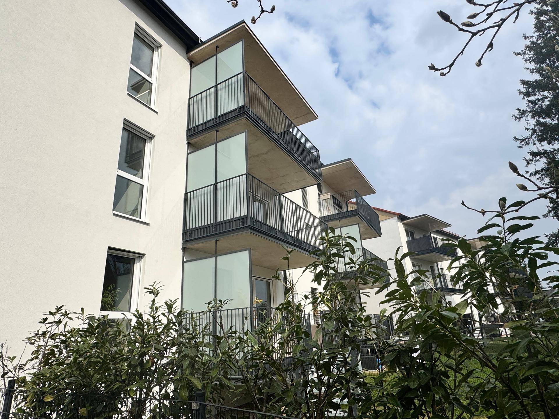 Wohngebäude mit moderner Architektur, Balkonen und gepflegter Grünanlage im Vordergrund.