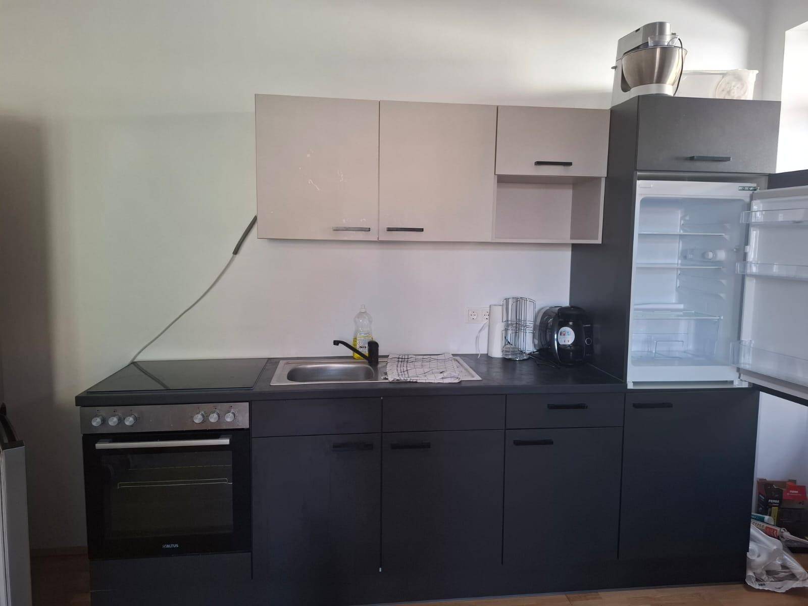 Kompakte Küche mit dunklen Unterschränken, hellen Oberschränken und integriertem Backofen.