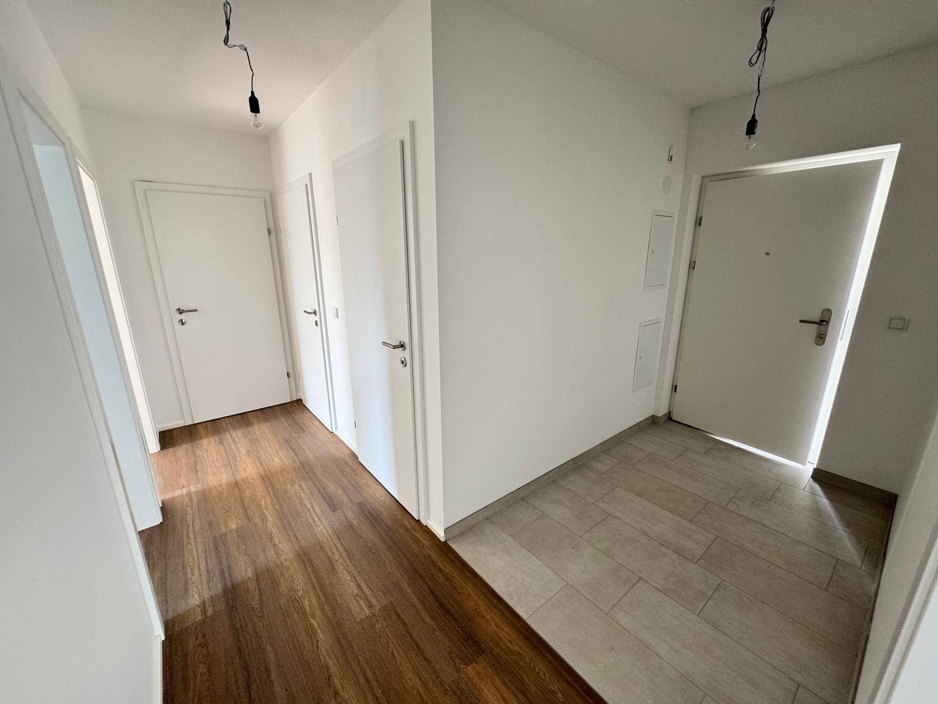Heller Flur mit zwei verschiedenen Bodenbelägen, Laminat und Fliesen, sowie mehreren weißen Türen.