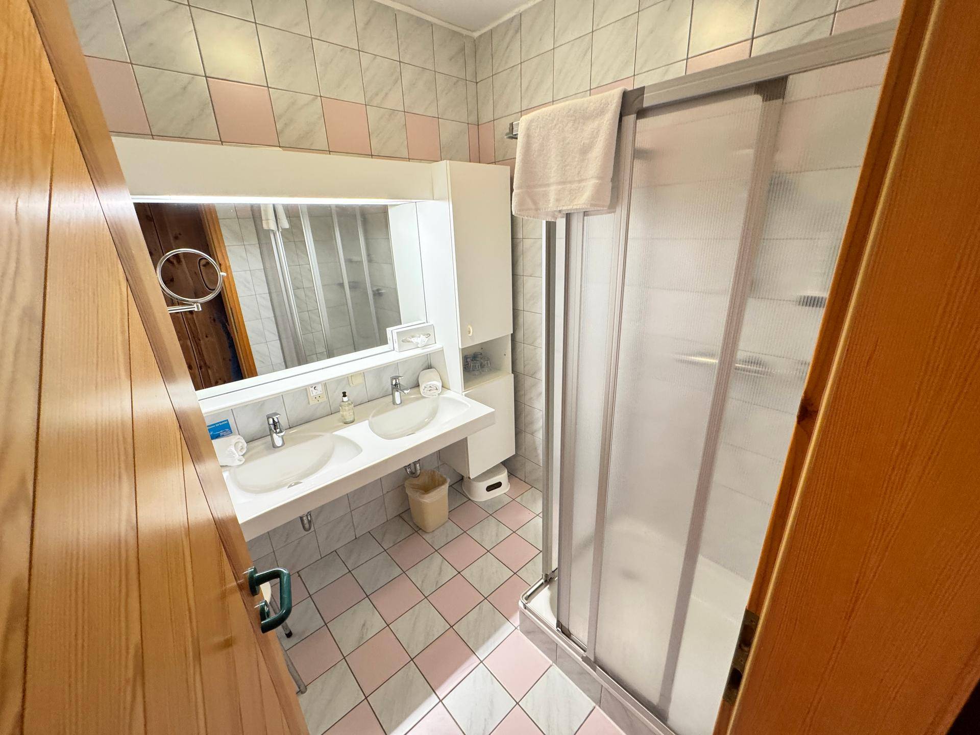 Badezimmer mit Doppelwaschbecken, Duschkabine und farbigen Fliesen.