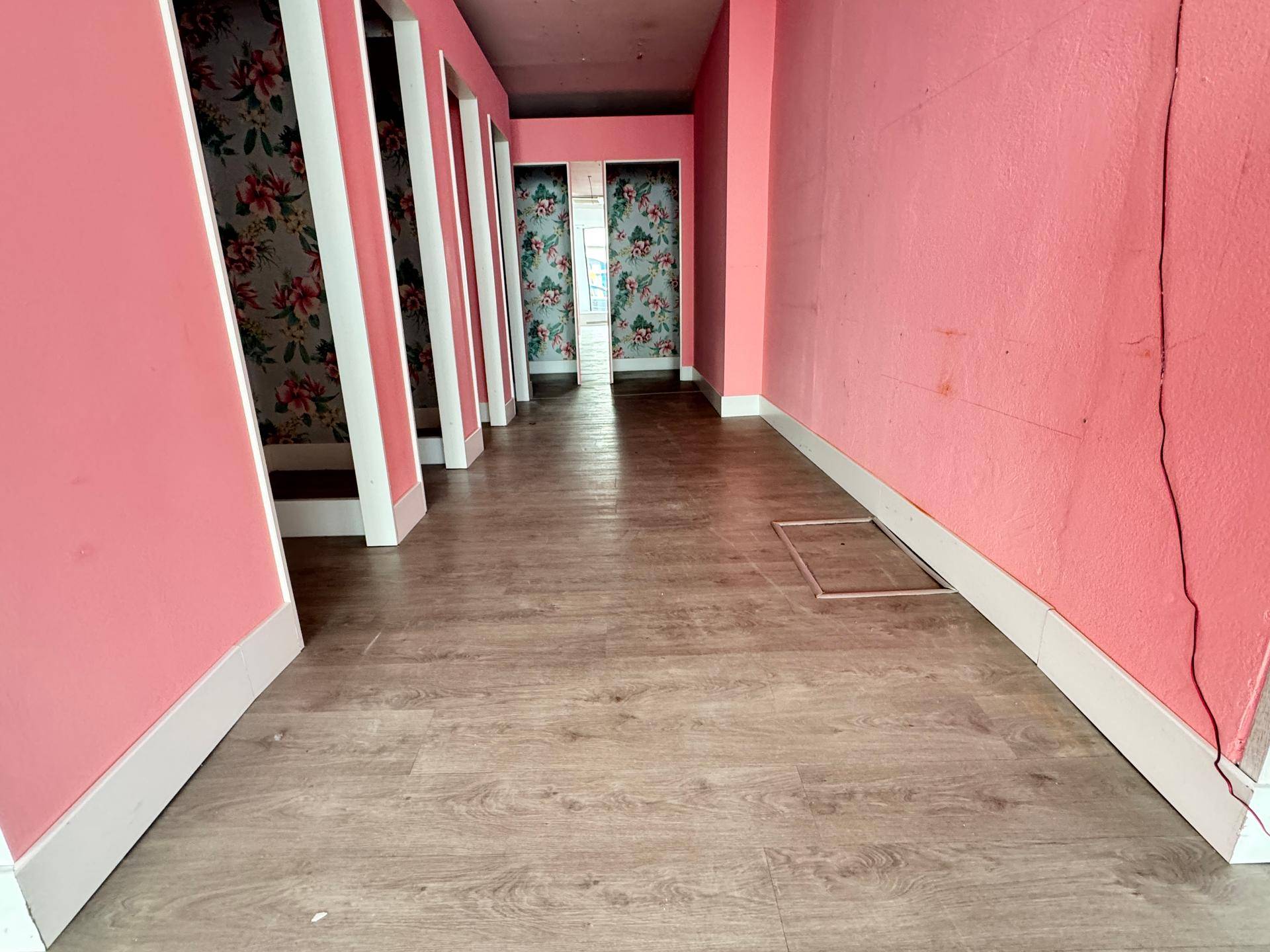Flur mit rosa Wänden und floraler Tapete in den Umkleidekabinen eines Ladenlokals.