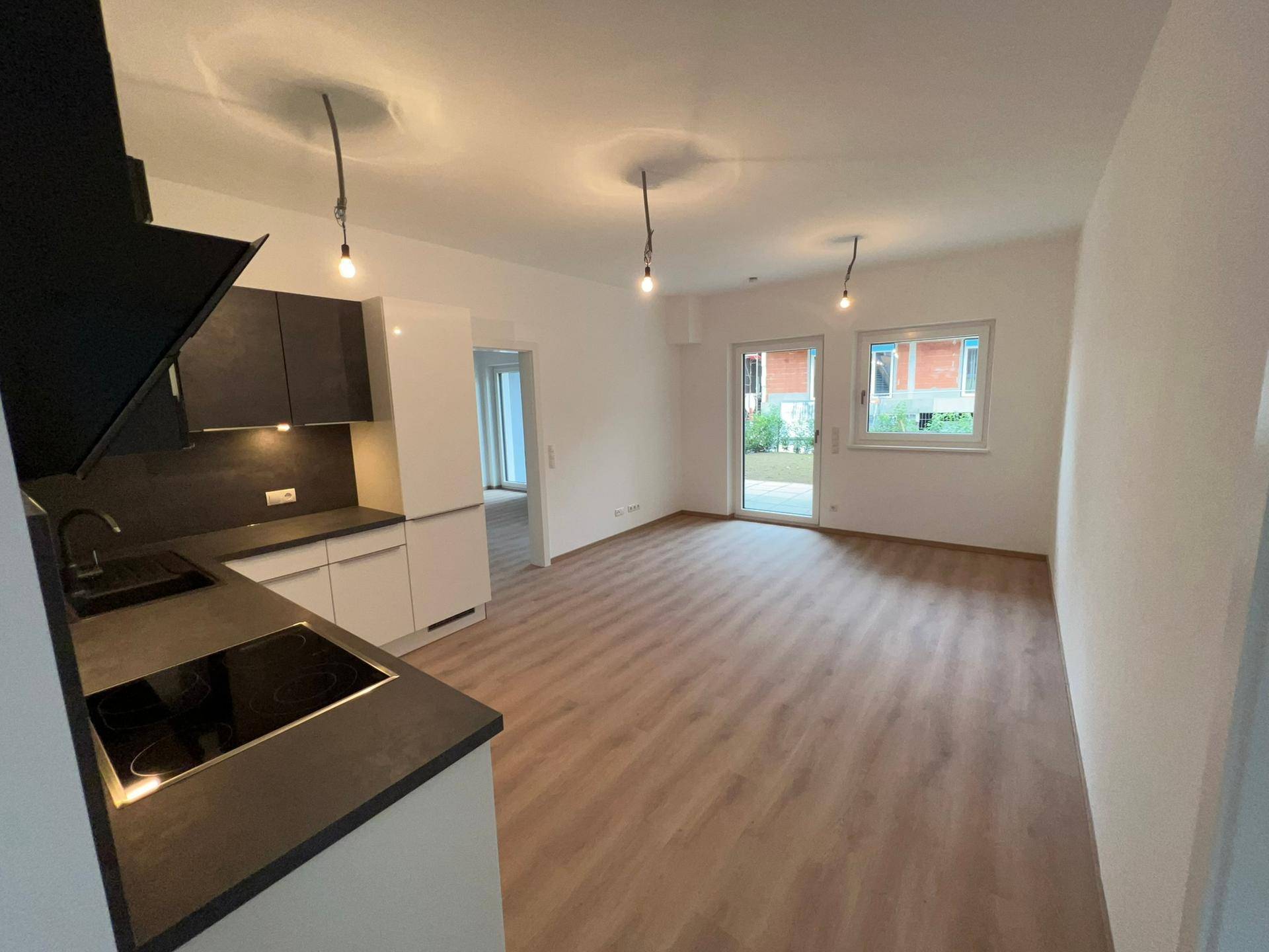 Offener Wohnbereich mit moderner Küche, Laminatboden und direktem Zugang zum Garten durch große Fenster.
