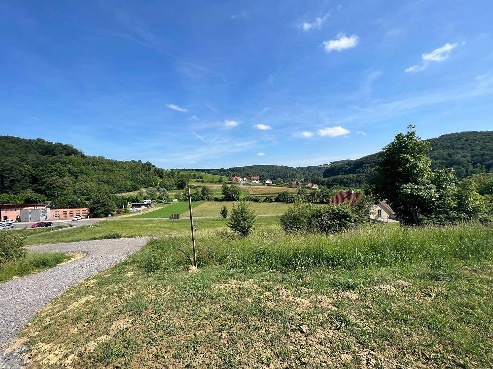 Panoramablick über eine weite, grüne Landschaft mit bewaldeten Hügeln und ländlicher Bebauung.