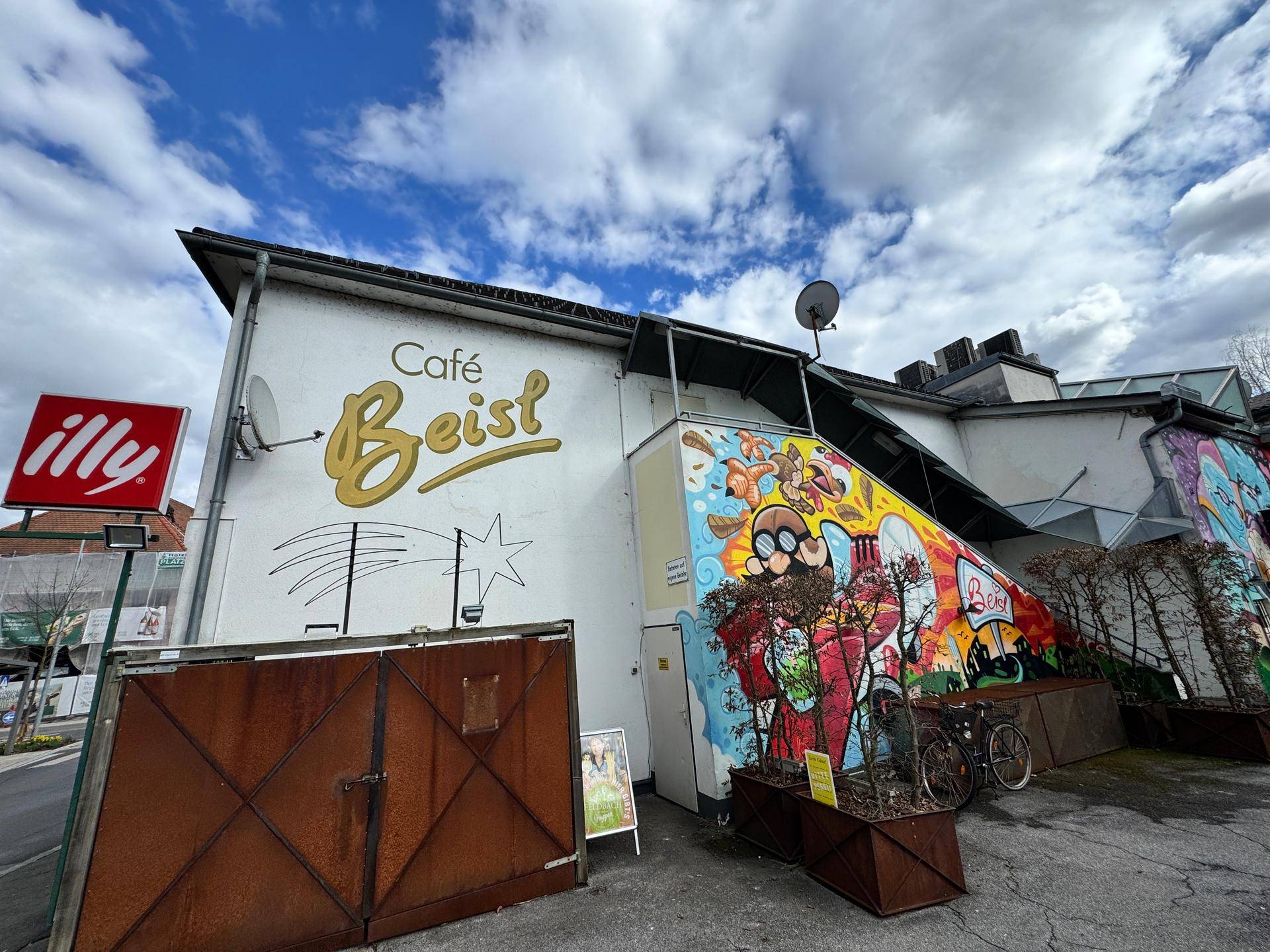 Gebäude mit farbenfrohem Graffiti an der Fassade und einem Außenbereich, der zu einem Café gehört.