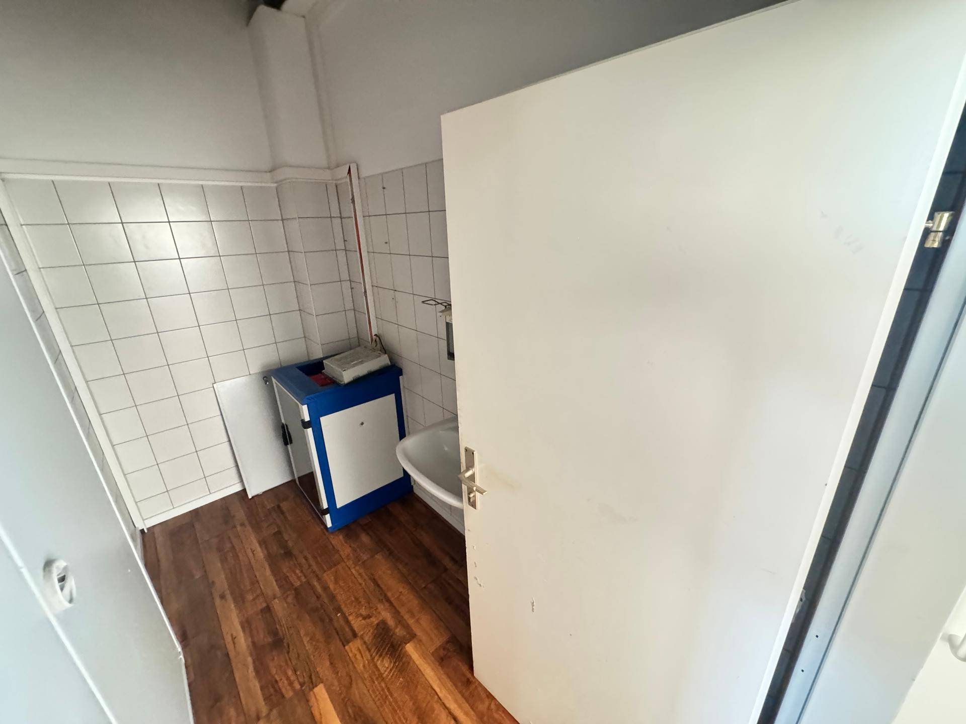 Kleiner Raum mit Holzboden und gefliesten Wänden, möglicherweise ein Abstellraum oder Technikbereich.