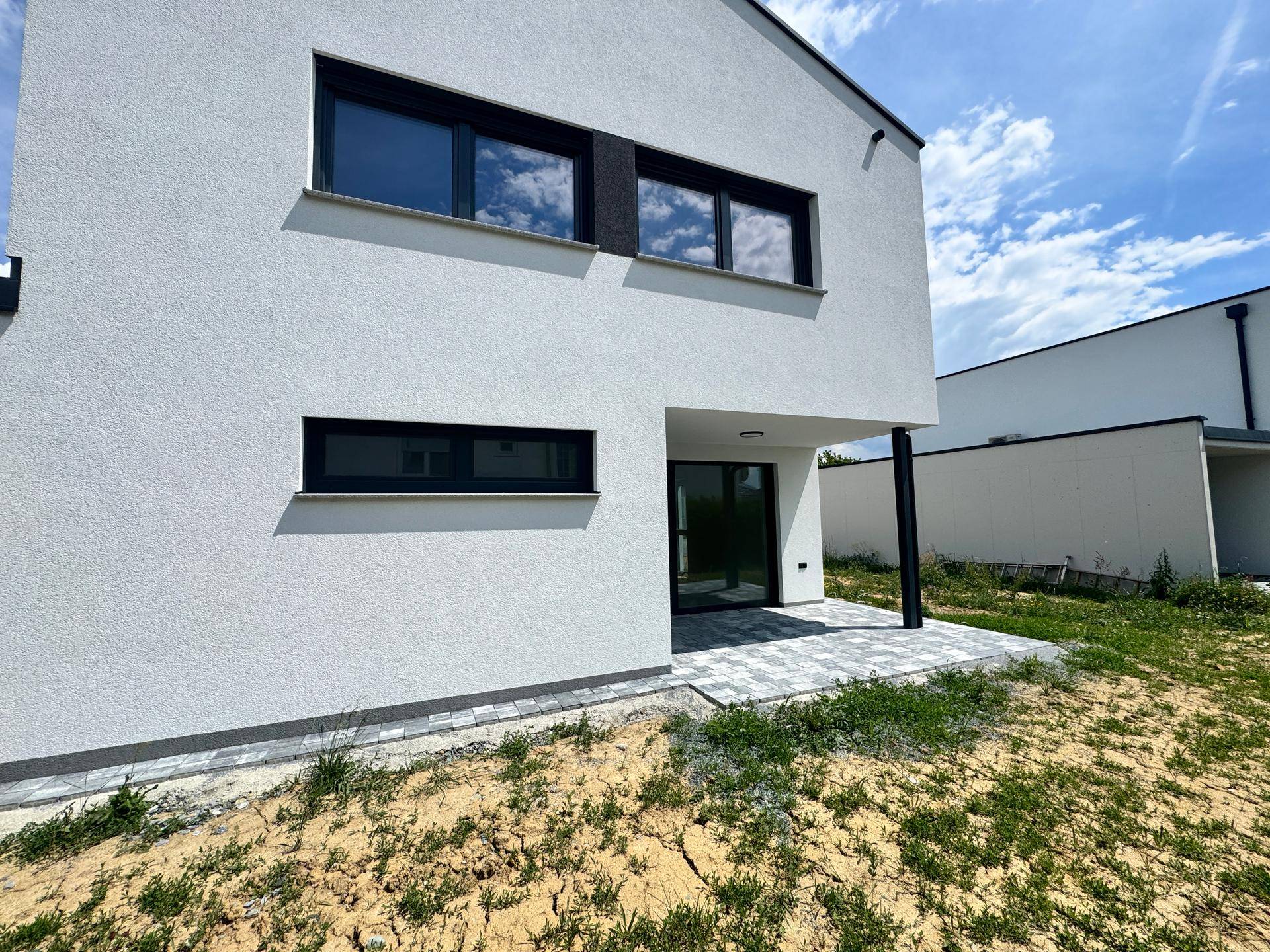 Rückseite des Hauses mit kleiner gepflasterter Terrasse und Zugang zum Gartenbereich.