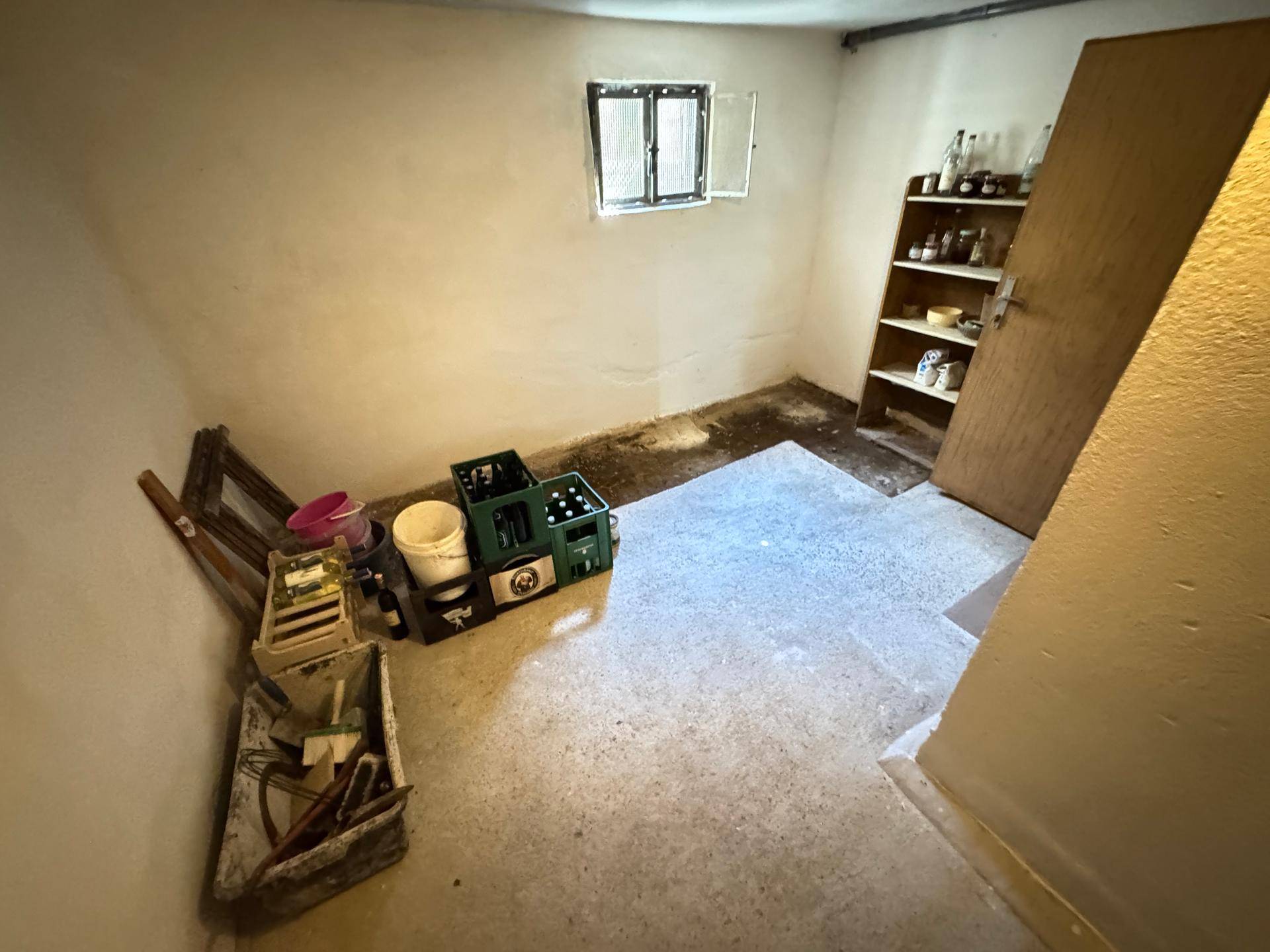 Lagerraum im Keller mit Regalen, Kisten und einem kleinen Fenster, das Tageslicht spendet.