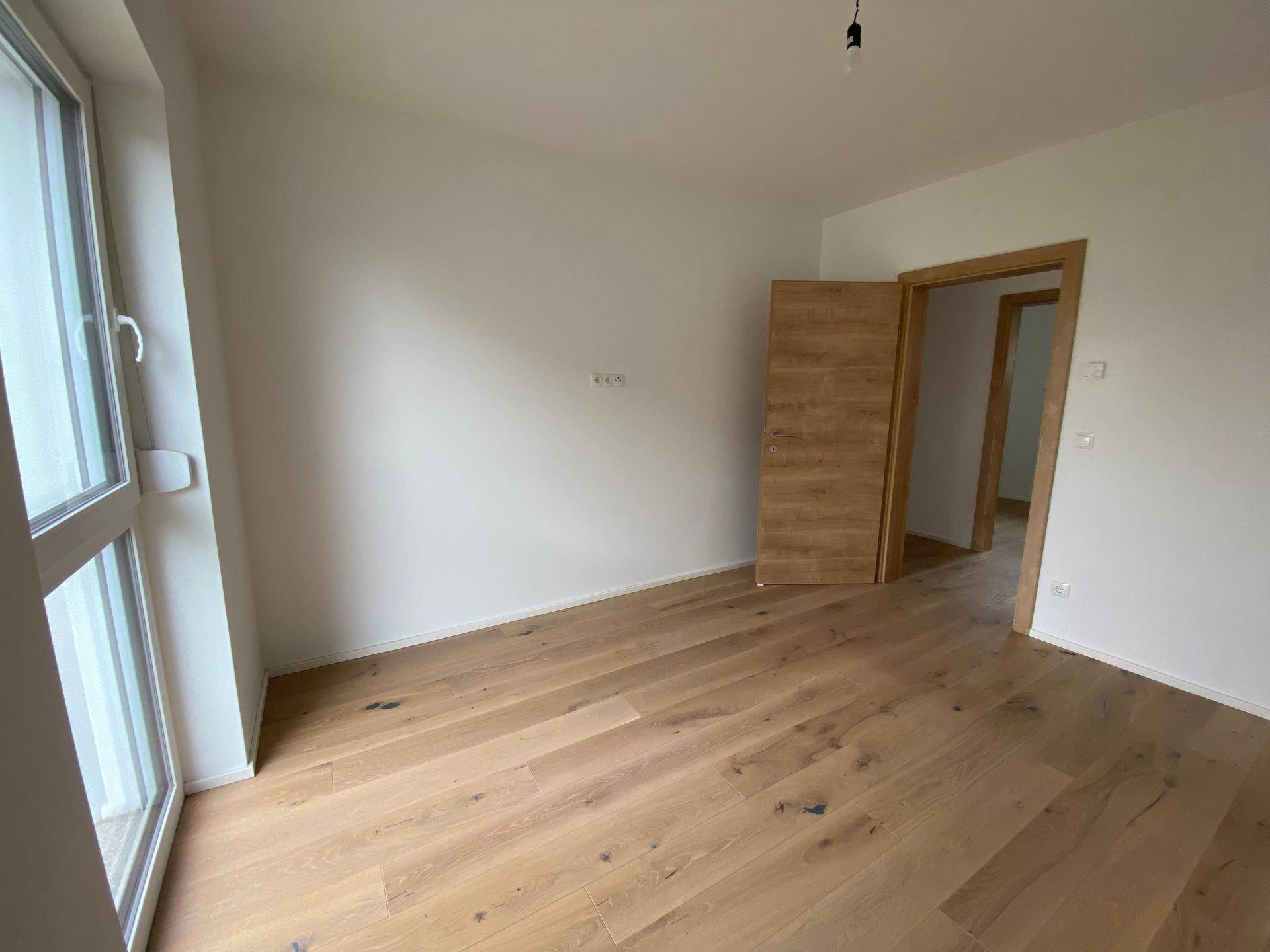 Helles Schlafzimmer mit Holzboden und großem Fenster, das viel natürliches Licht spendet.