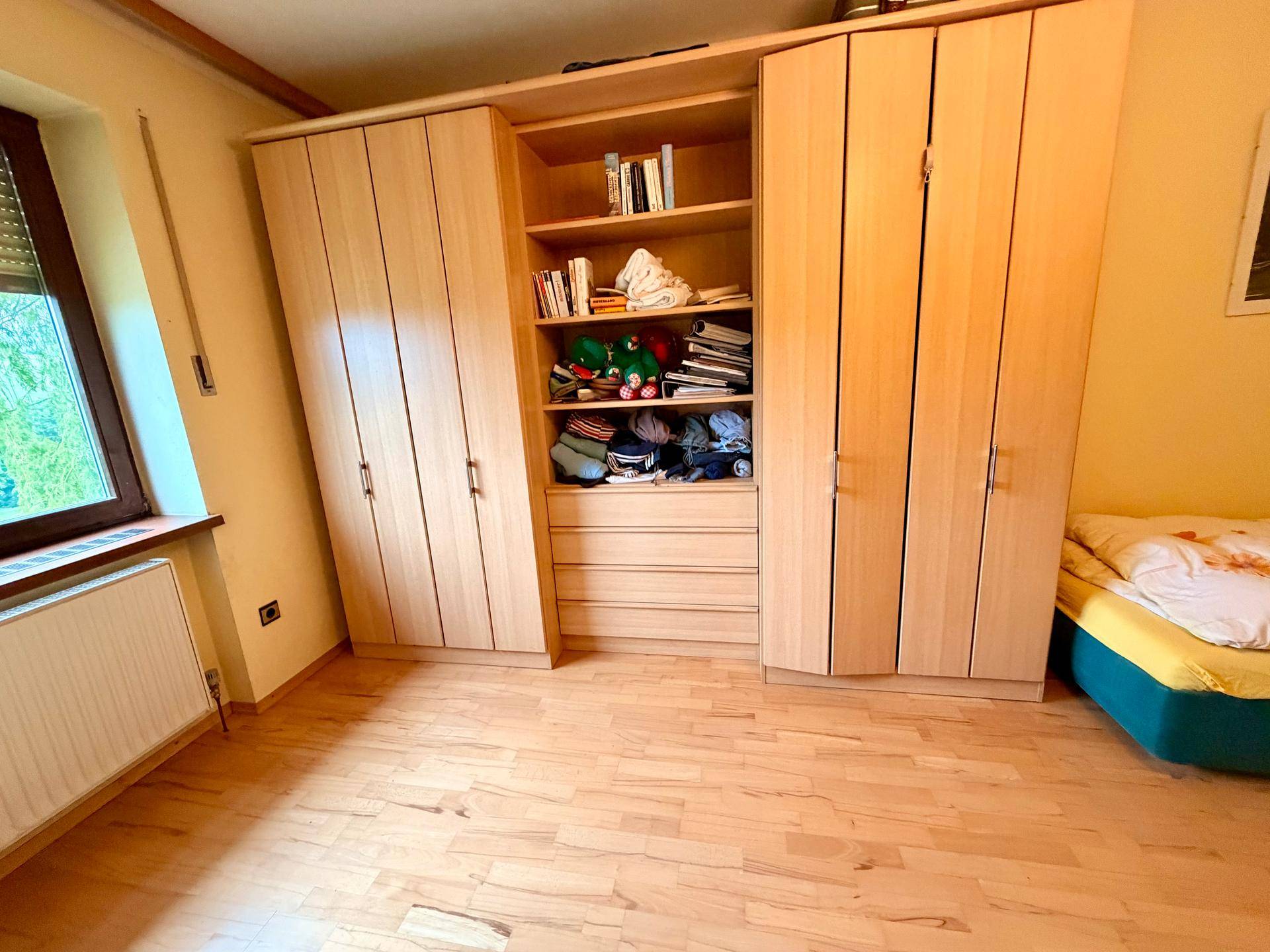 Schlafzimmer mit geräumigen Holzschränken und Fenster, bietet viel Stauraum.