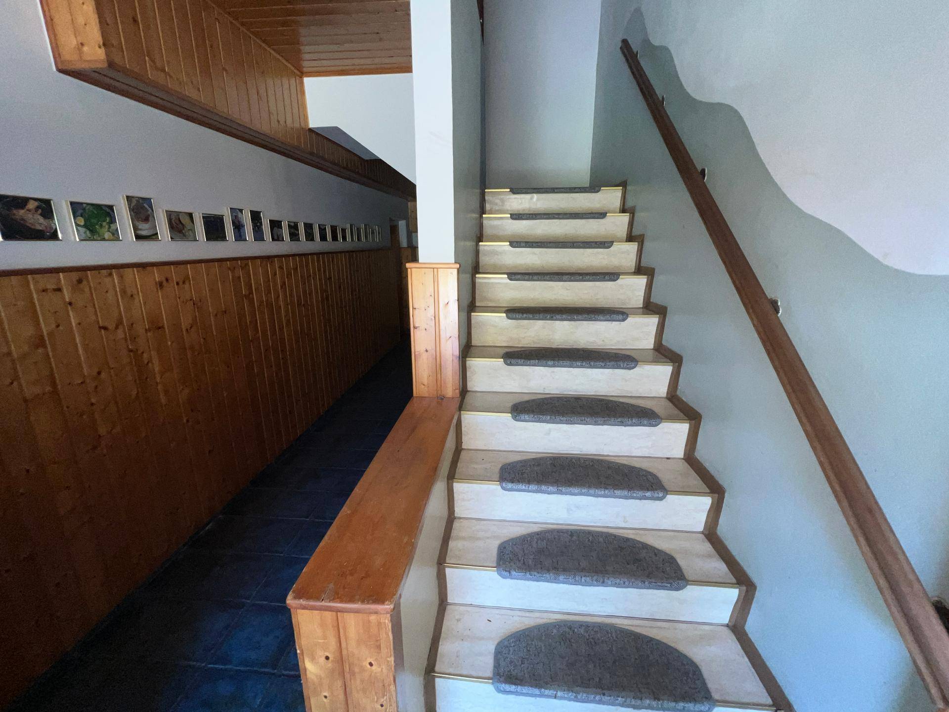 Holztreppe mit Teppichläufern und Holzvertäfelung an den Wänden, führt in die obere Etage.