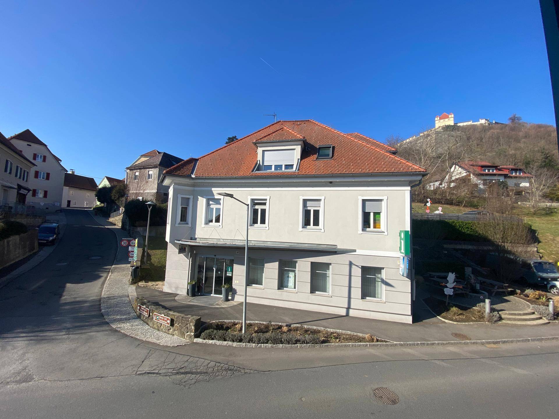 Gebäude an einer Straßenecke mit Blick auf eine Burg auf dem Hügel im Hintergrund.