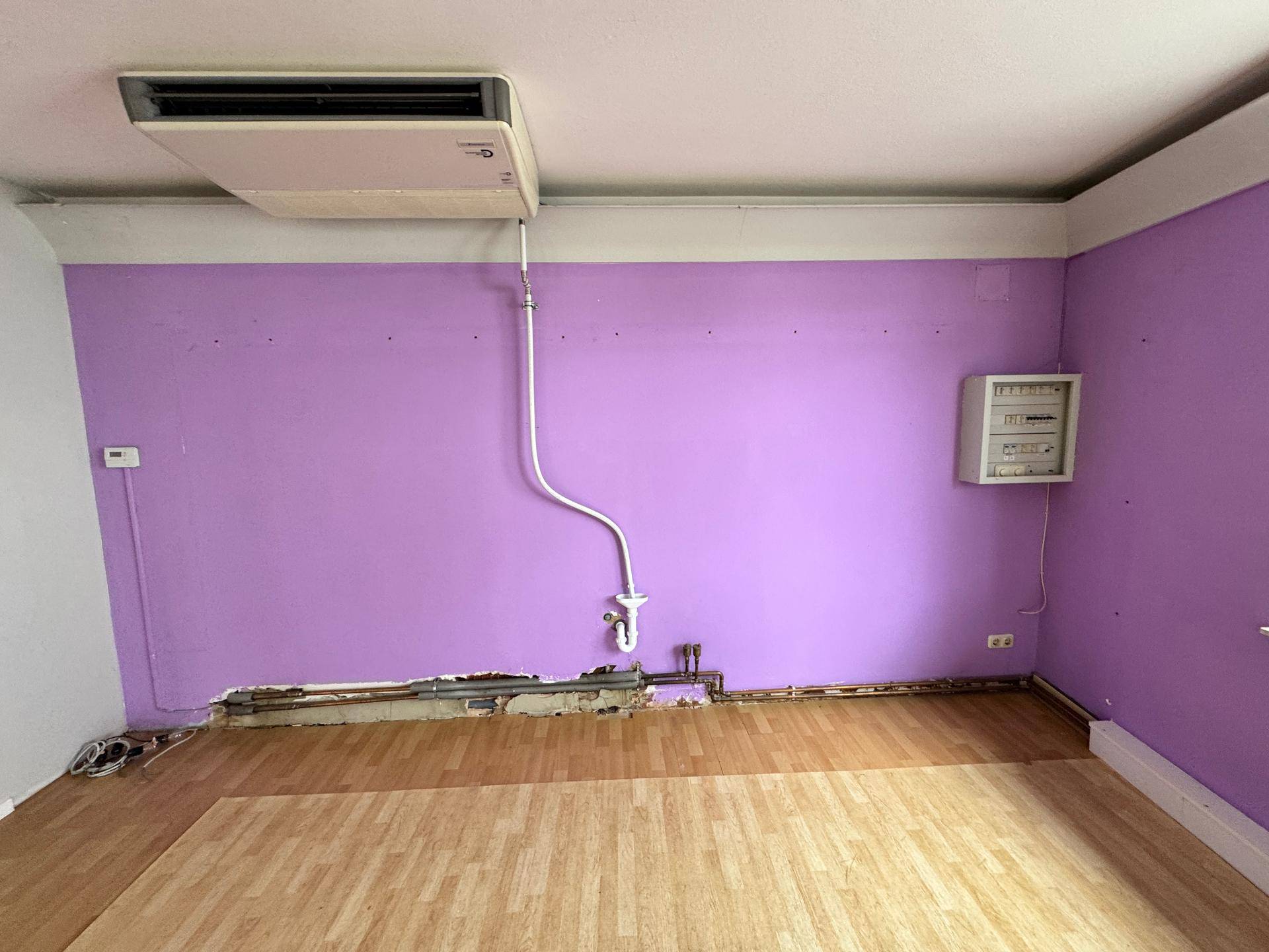 Bereich eines Raumes mit lila Wand, sichtbaren Rohren und einem elektrischen Verteilerkasten.