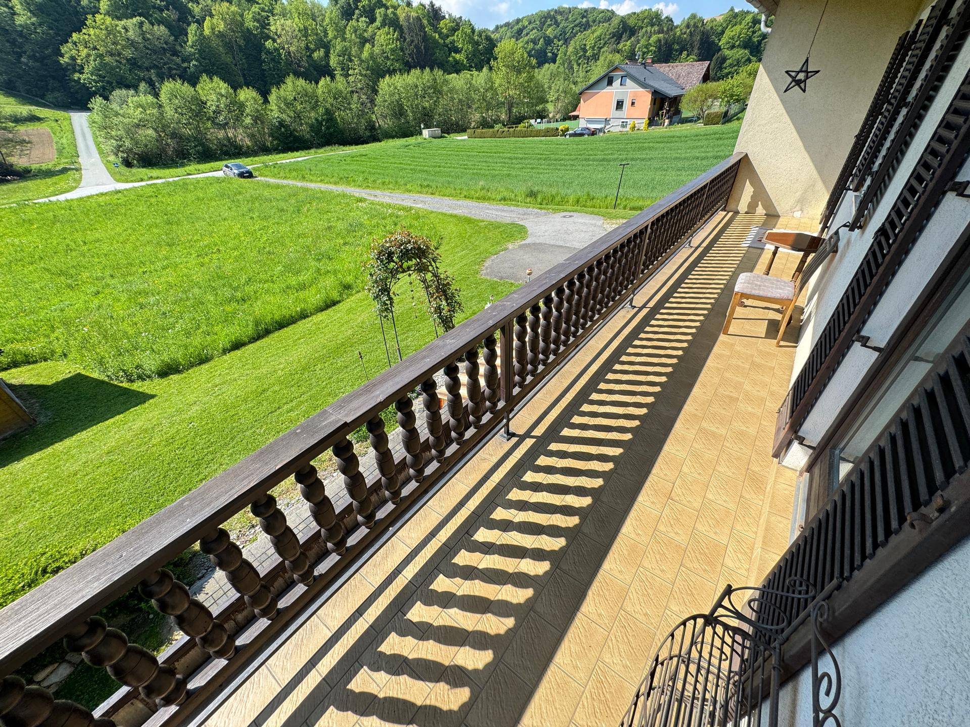 Langer Balkon mit Holzgeländer und weitem Blick über grüne Felder und die Landschaft.