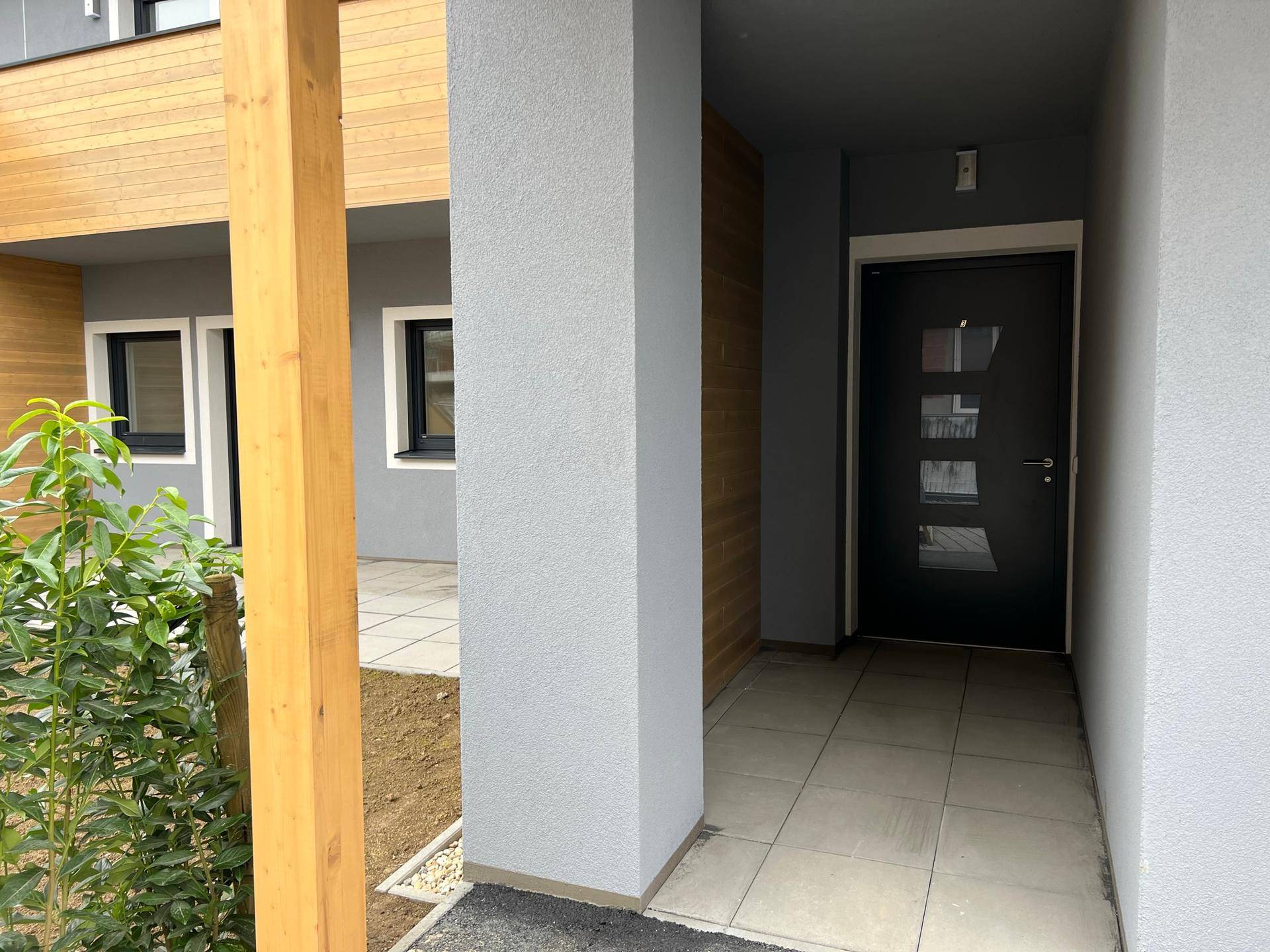 Eingangsbereich eines Neubaus mit moderner Haustür, Holzelementen und gepflastertem Zugang.